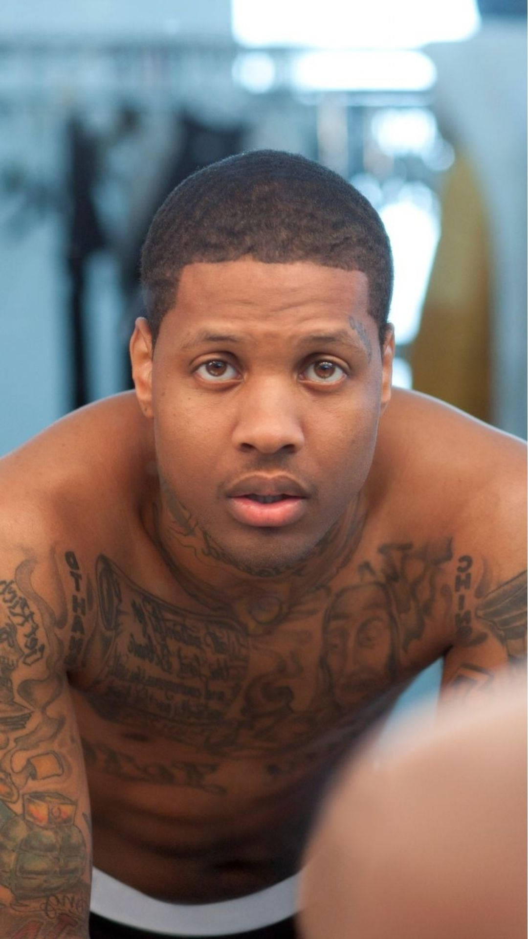 Lil Durk 桌布 壁紙 — 一個赤裸上身的男子，身上有大量刺青，在燈光明亮的健身房中，專注地凝視著鏡頭。