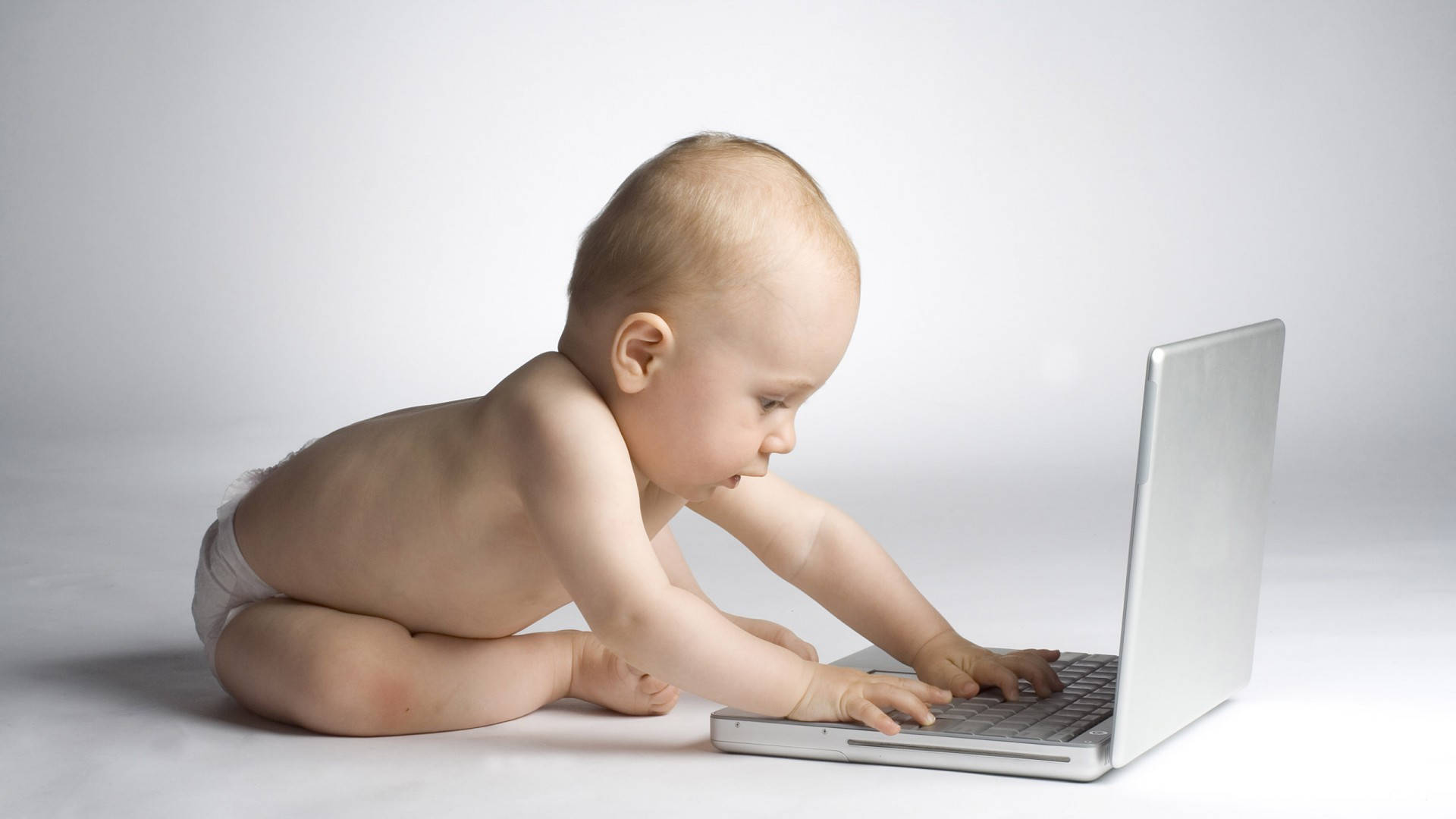 Funny Baby 桌布 壁紙 — 一個赤裸上身穿尿布的嬰兒坐在白色地板上，專注地在銀色筆記型電腦上打字。