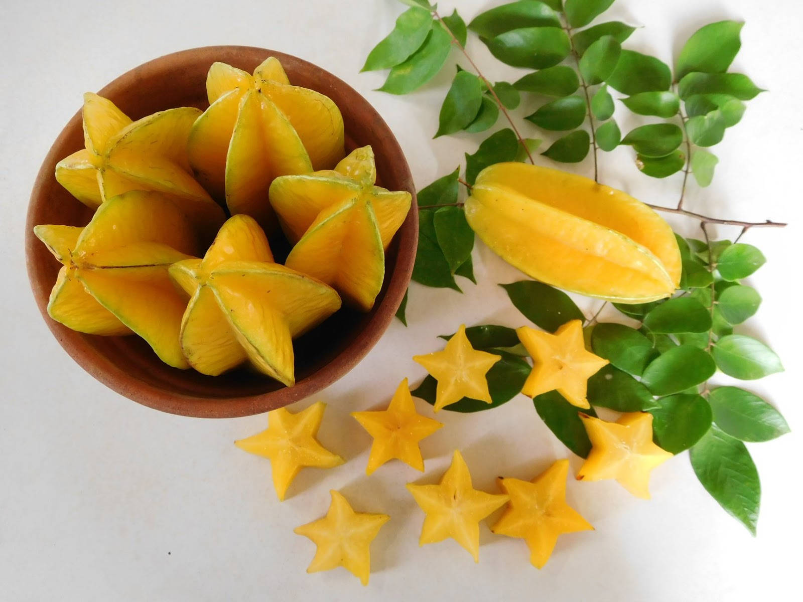 Fruit 桌布 壁紙 — 一個赤陶碗盛載著鮮黃色的楊桃，配上新鮮綠葉和切片，散落在白色表面上。