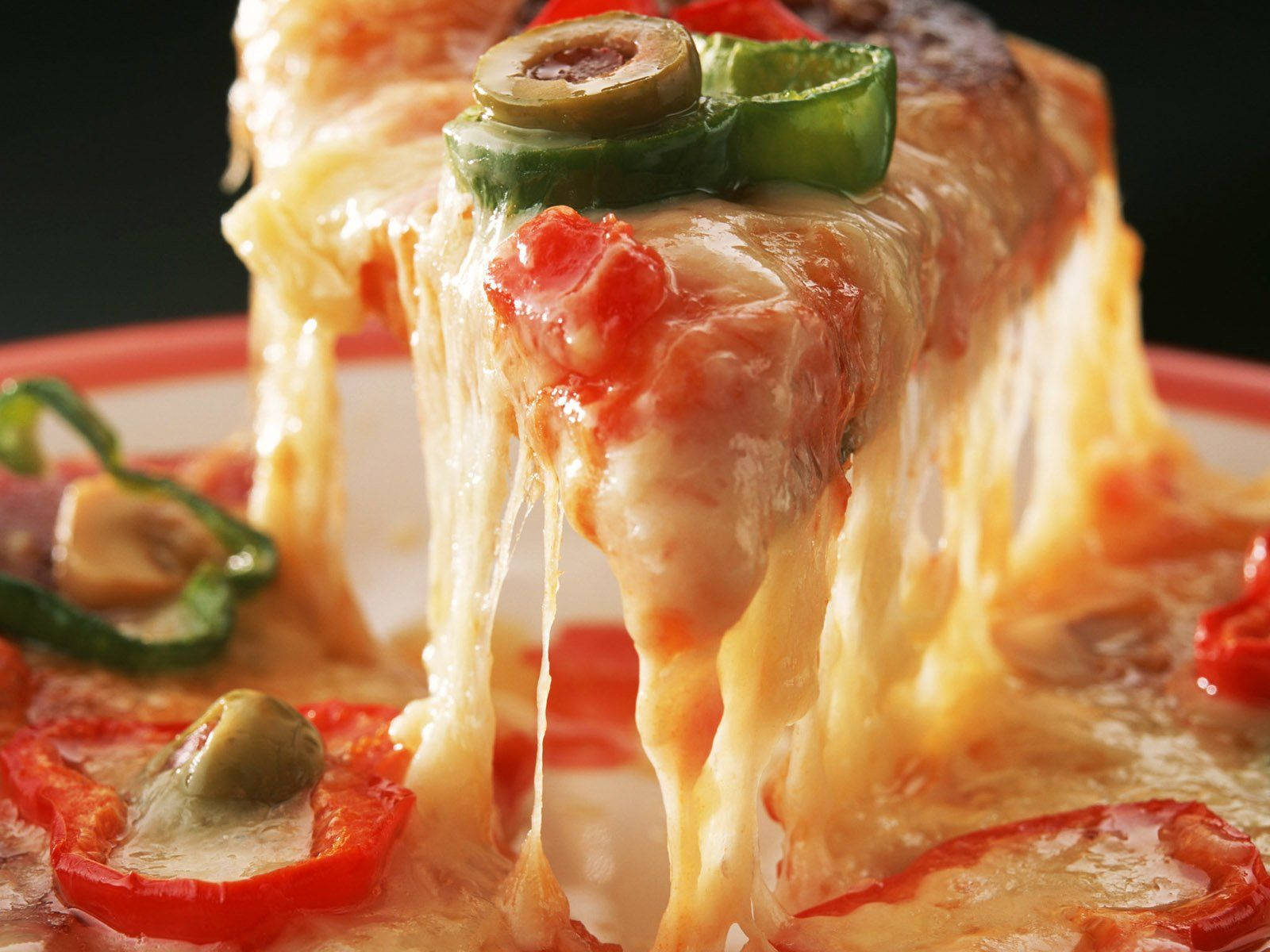 Dominos Pizza 桌布 壁紙 — 一個起司披薩片的特寫，融化起司向下拉長，上面有青橄欖和紅椒。
