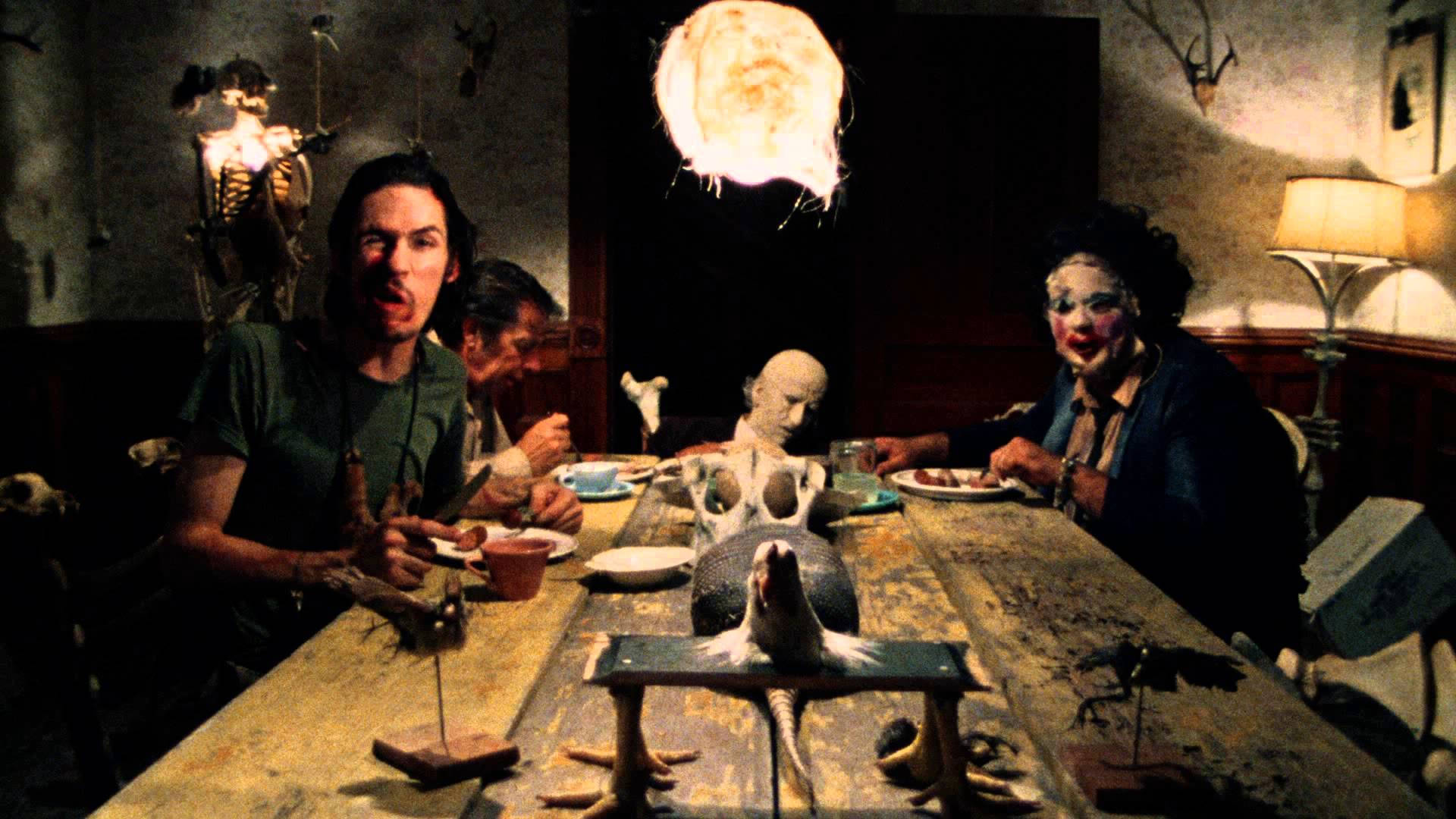Texas Chainsaw Massacre 桌布 壁紙 — 一個超現實的晚餐場景，有怪誕的人物和一個漂浮的球體，在一個燈光昏暗、雜亂的房間裡。