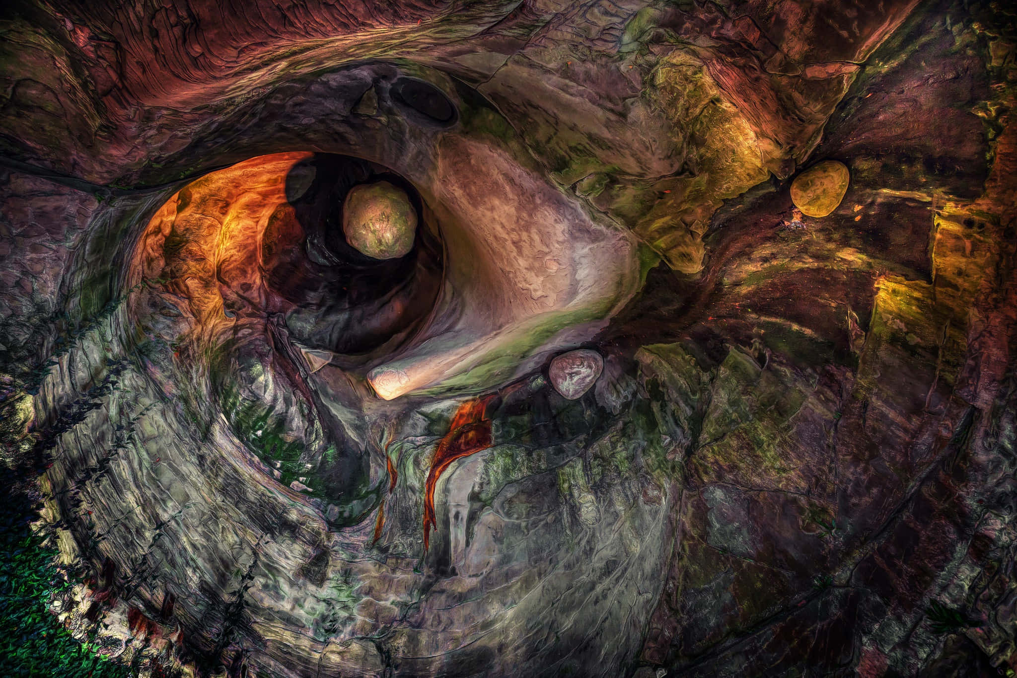Geomorphology 桌布 壁紙 — 一個超現實的洞穴內部，在戲劇性的燈光下，旋轉的岩石結構散發出溫暖的橙色和涼爽的綠色色調。