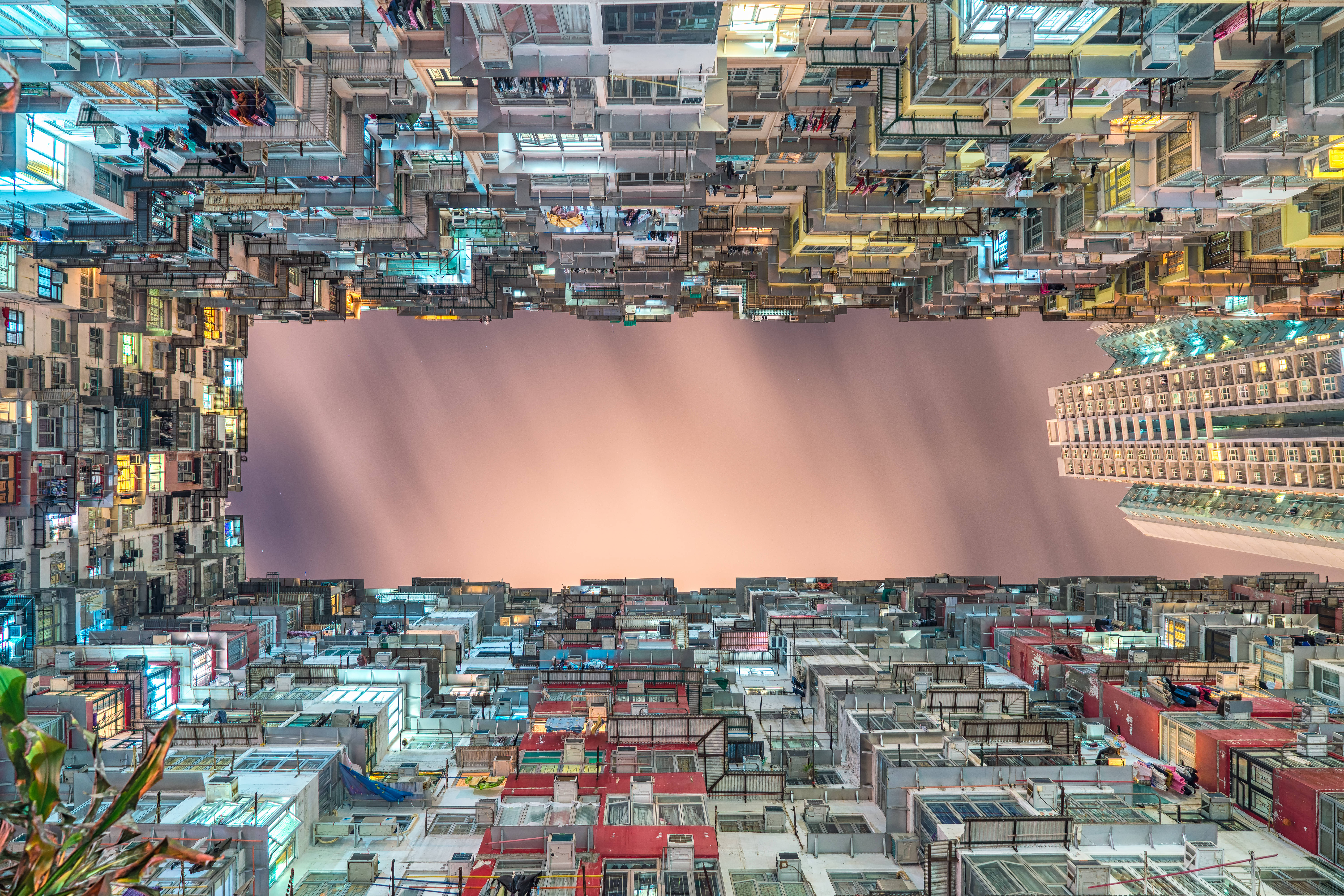 香港 桌布 壁紙 — 一個超現實的顛倒城市景觀，密集的建築物和發光的窗戶映襯著柔和的粉紅色天空。