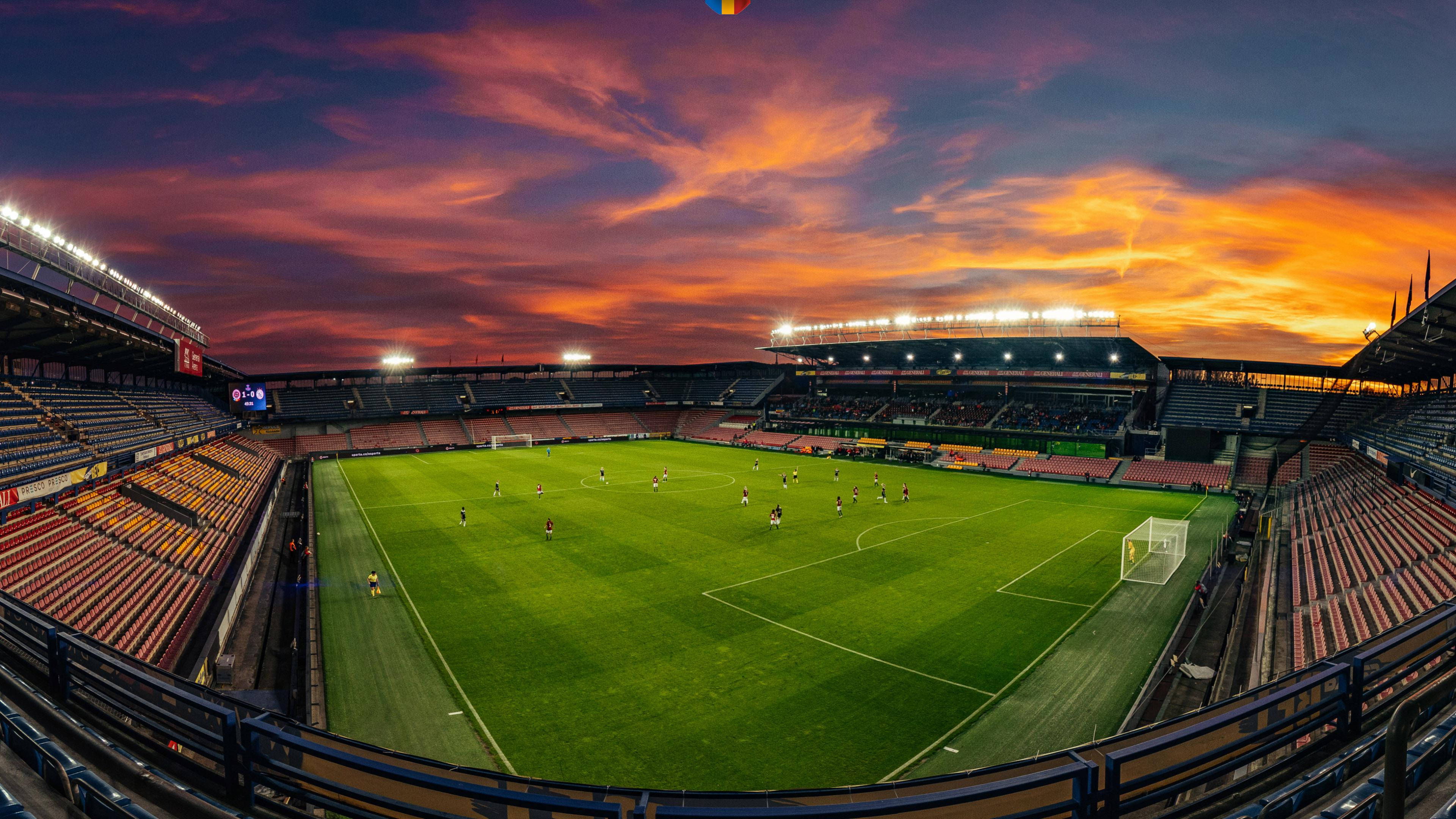 Stadium 桌布 壁紙 — 一個足球場在日落時分，球員在球場上，天空呈現鮮豔的橙色和紫色。