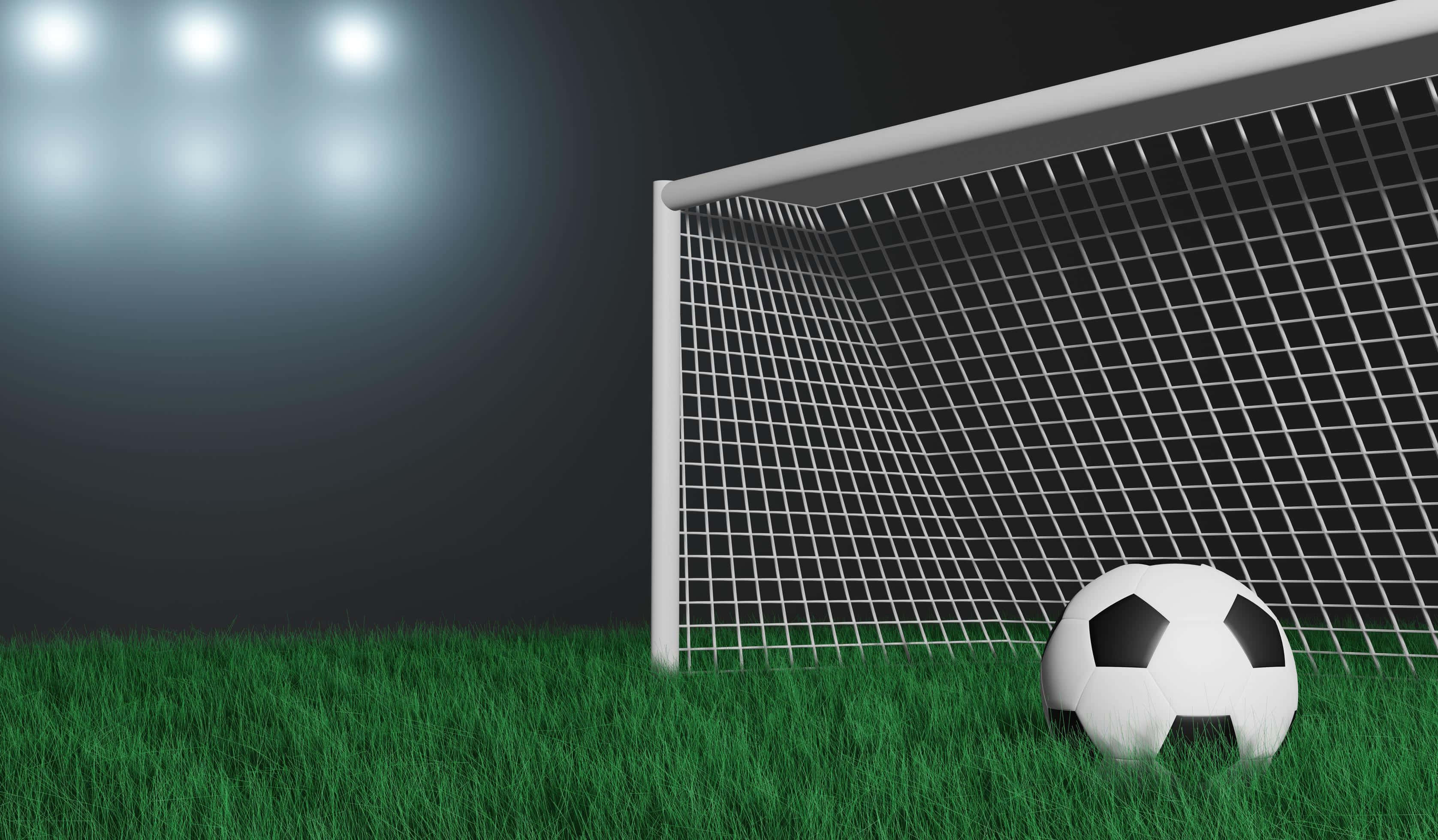 Football Field 桌布 壁紙 — 一個足球放在鮮綠色草地上，前面是白色球門網，夜晚球場燈光璀璨。