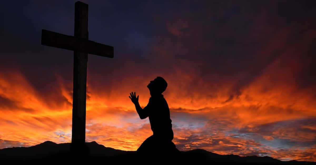Gospel 桌布 壁紙 — 一個跪著的人物在木製十字架旁祈禱，背景是帶有戲劇性雲彩的熾熱日落天空。