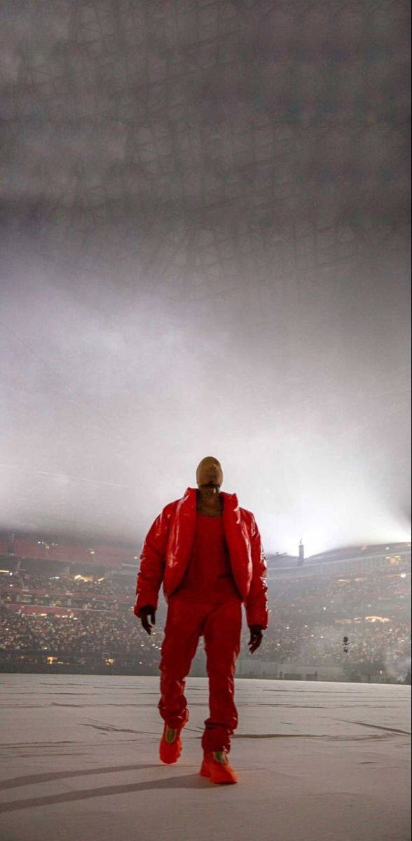 Kanye 桌布 壁紙 — 一個身穿亮紅色西裝的人影獨自走在廣闊的體育場舞台上，天空迷濛昏暗。