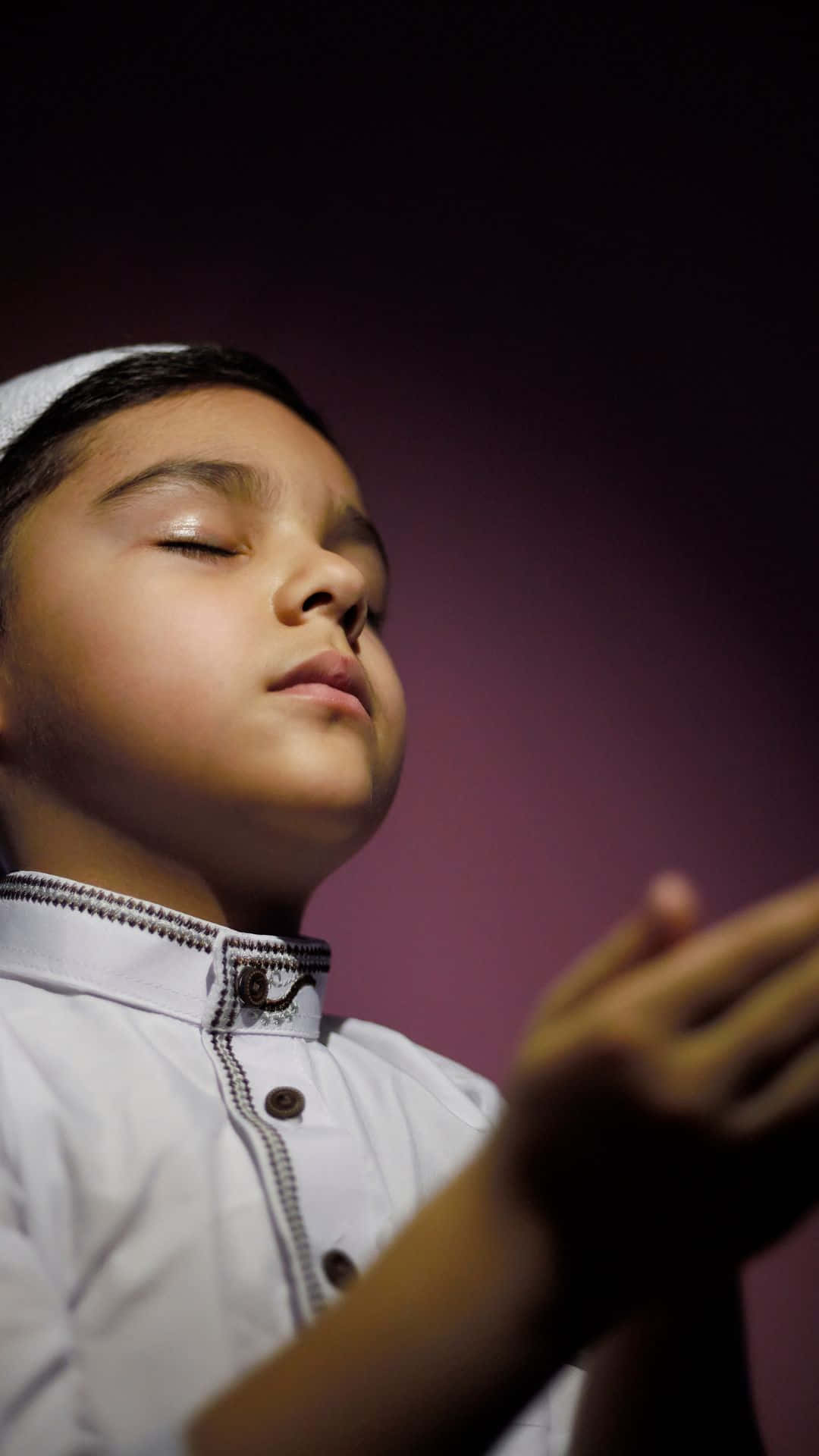Praying 桌布 壁紙 — 一個身穿傳統白色服裝的小男孩，在深紫色漸層背景前閉眼祈禱。