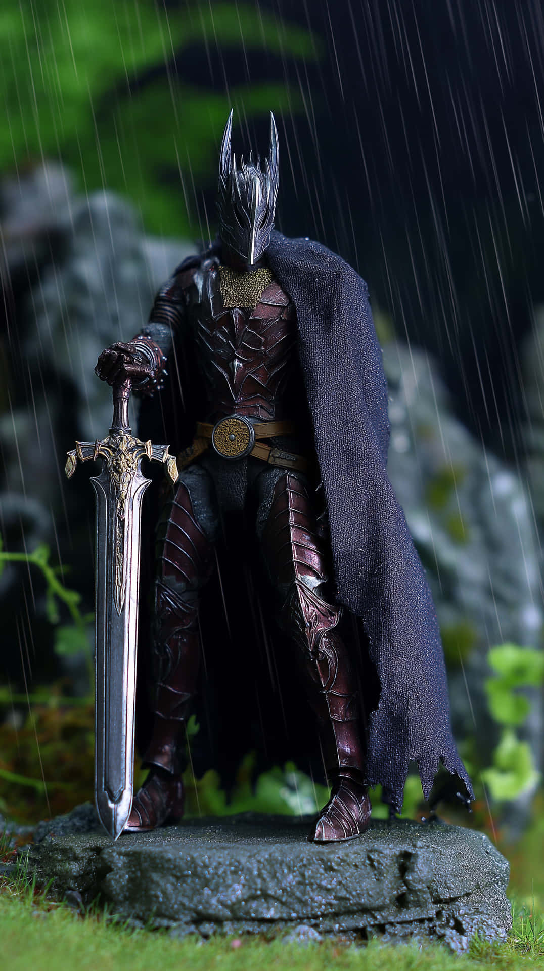 Regal Dark Knight in Ornate Armor Amidst Gentle Rain 壁紙 — 一個身穿深色盔甲、頭戴尖刺頭盔、披風飄揚的戰士，在雨中站在長滿苔蘚的石頭上，手持一把巨大的華麗劍。
