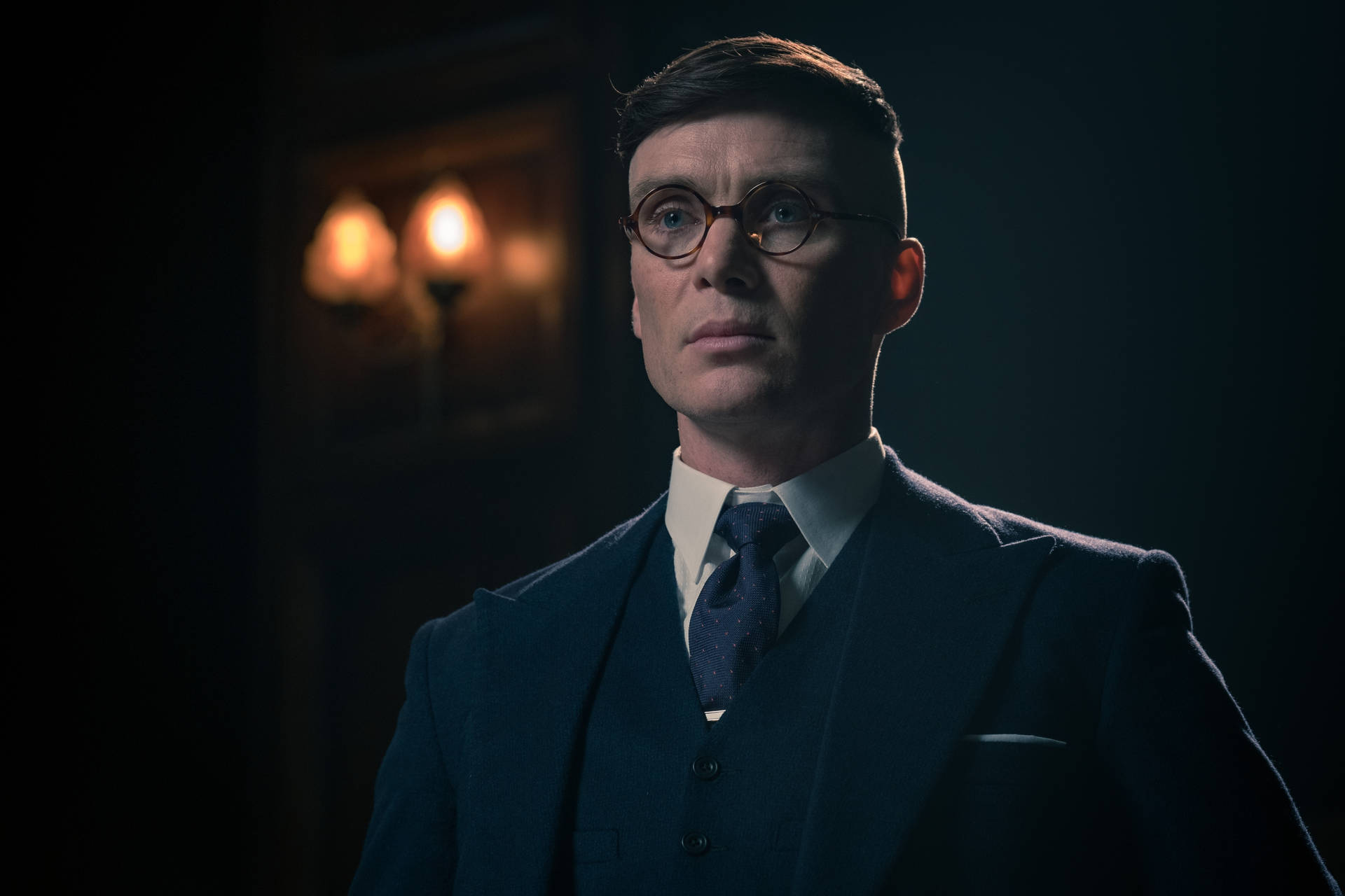深色西裝圓框眼鏡男人，昏暗房間，溫暖壁燈。 — Peaky Blinders 壁紙