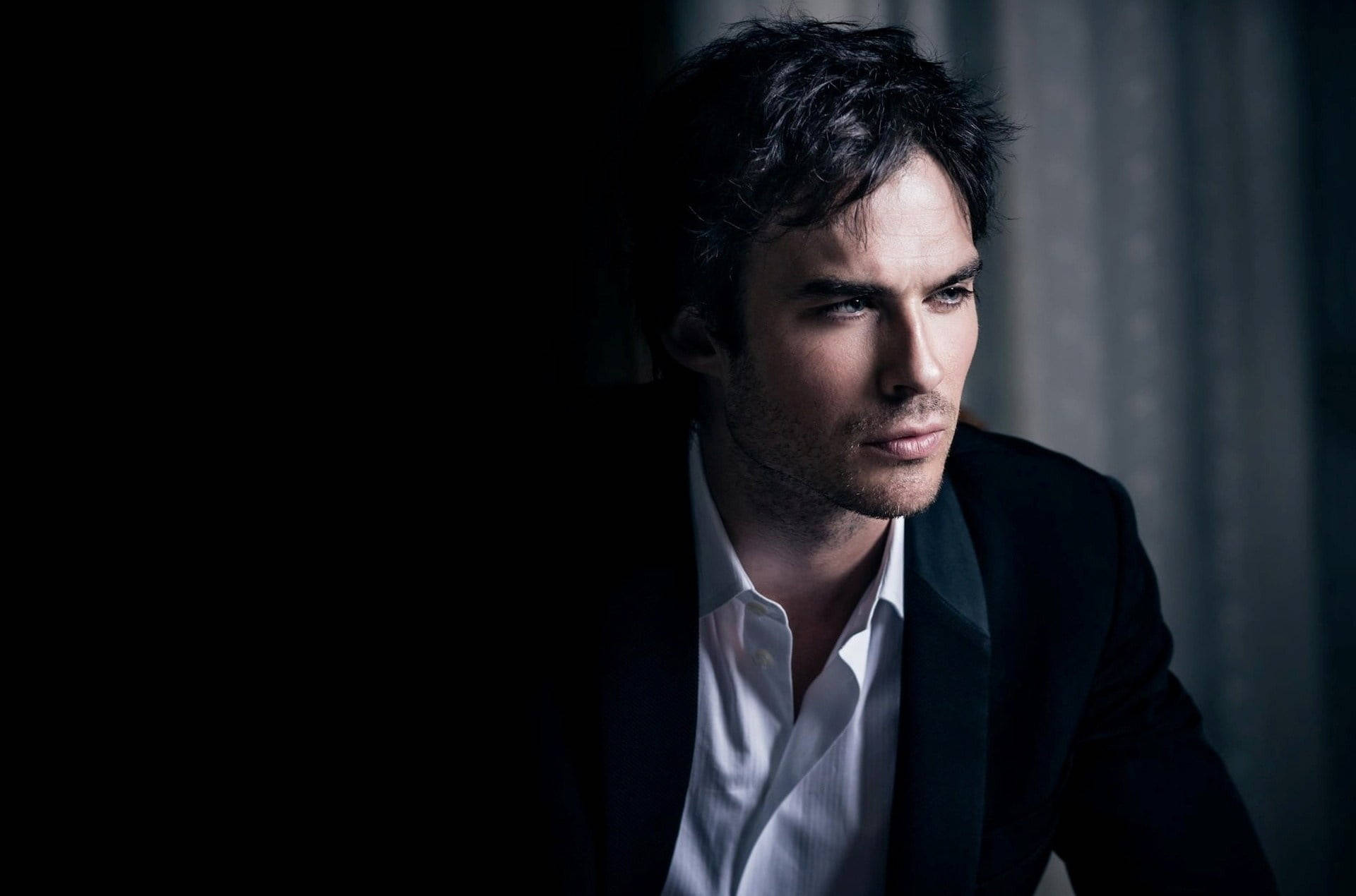 Ian Somerhalder 桌布 壁紙 — 一個身穿深色西裝和白色襯衫的男人在昏暗燈光下帶著戲劇性的陰影沉思地凝視。