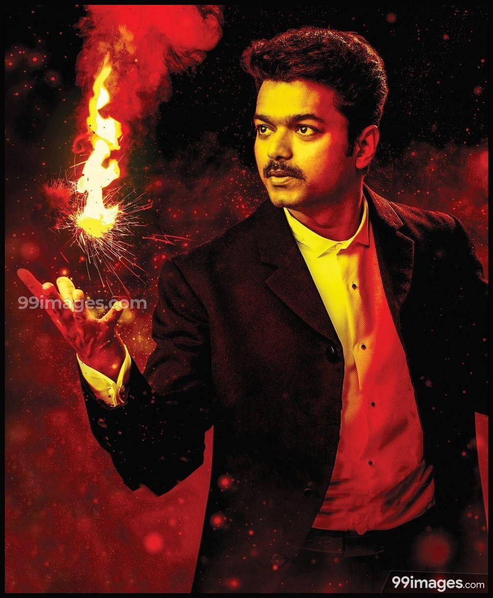 vijay HD 桌布 壁紙 — 一個身穿深色西裝的男人，在熾熱的紅色宇宙背景下手持閃爍的煙火。
