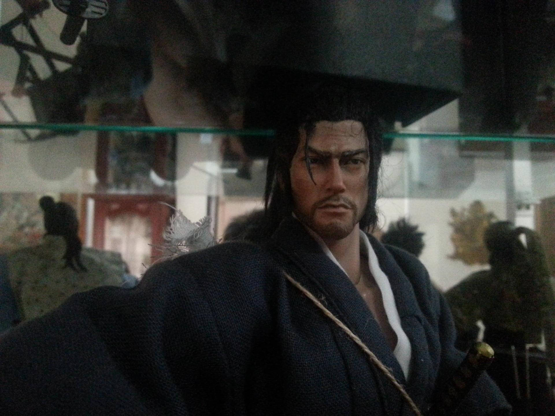 Vagabond 桌布 壁紙 — 一個身穿深藍色長袍、腰間佩劍的精細武士人偶，透過玻璃展示櫃凝視著。