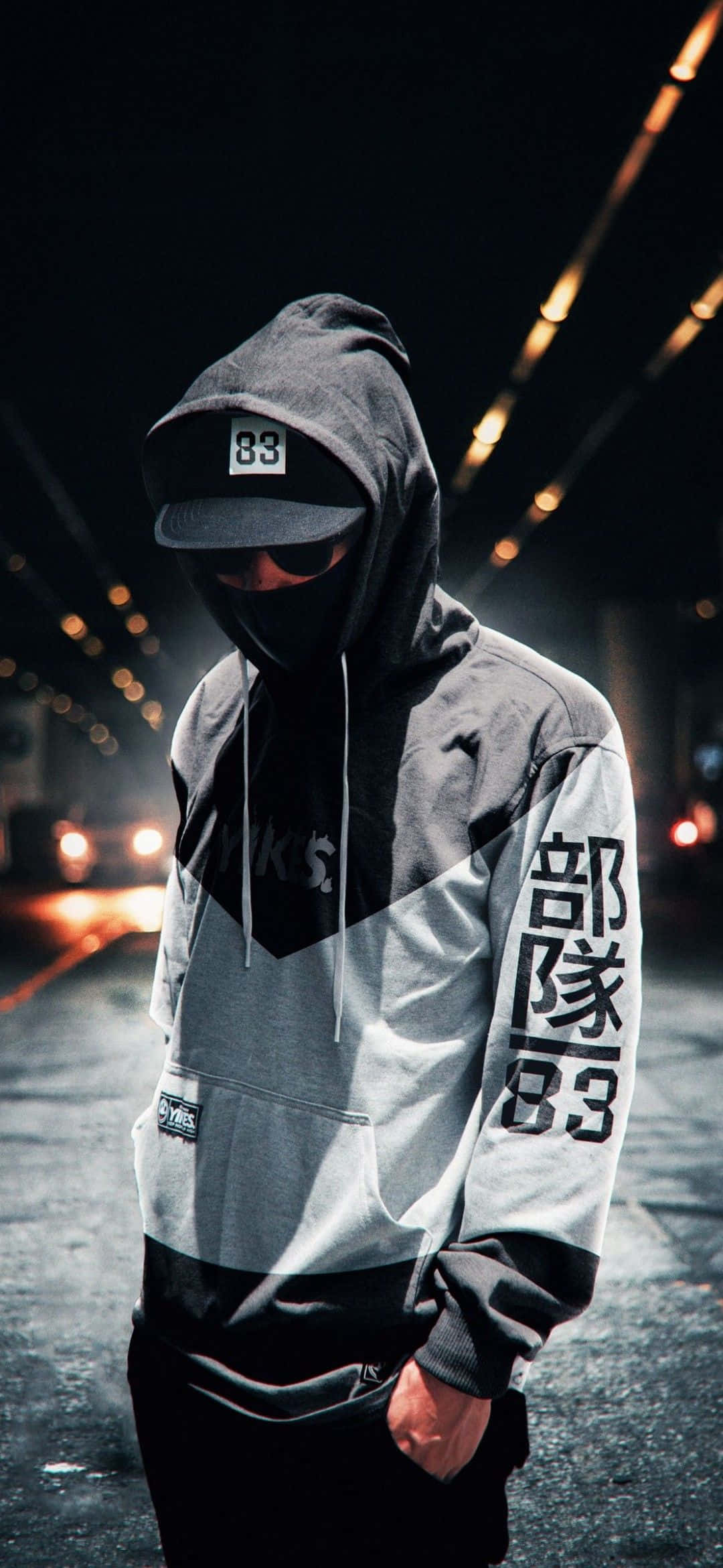 Mask Boy 桌布 壁紙 — 一個身穿灰色連帽衫、帶有'83'和漢字的蒙面人物，站在一個由溫暖發光燈光照亮的黑暗城市隧道中。