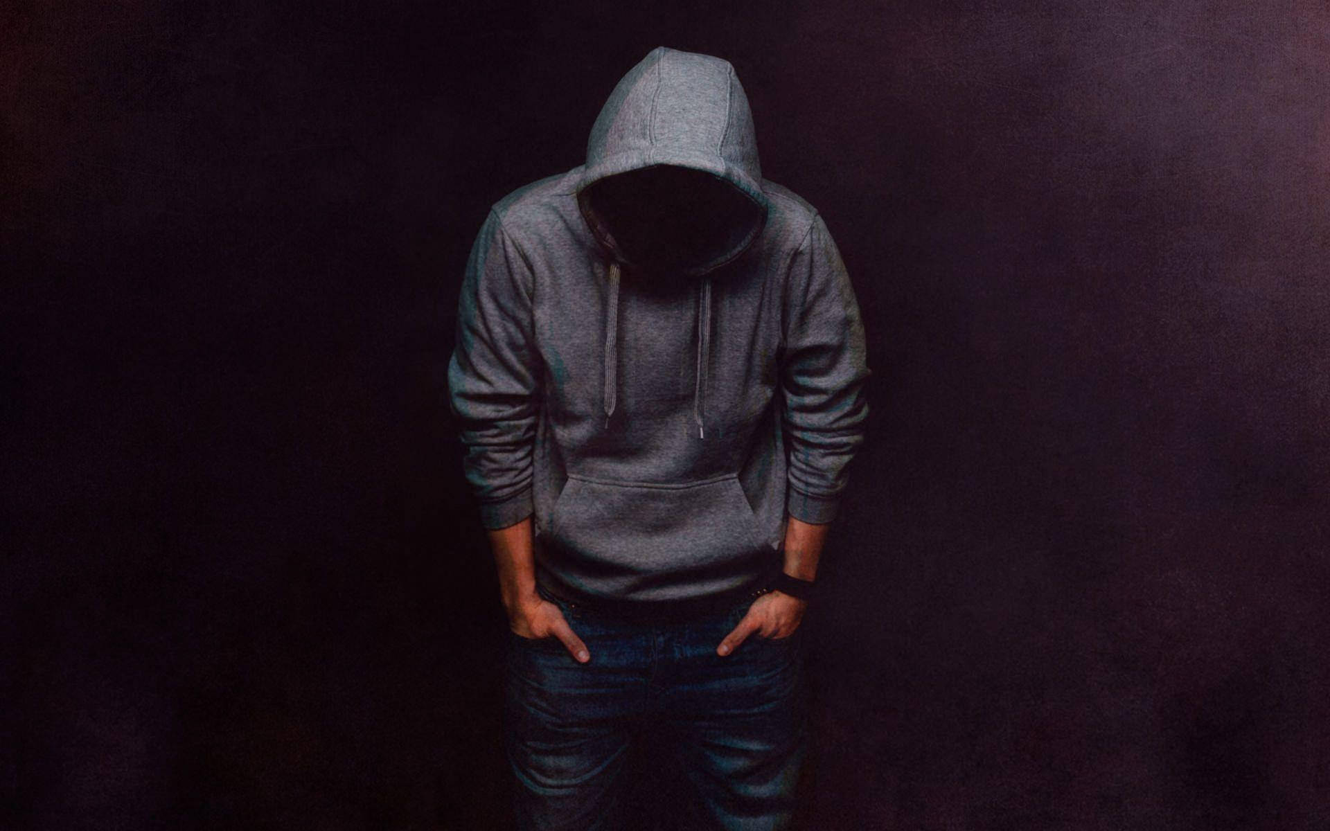 Hoodie 桌布 壁紙 — 一個身穿灰色連帽衫、臉部隱藏的人，雙手插袋，站在昏暗的紫色燈光中。