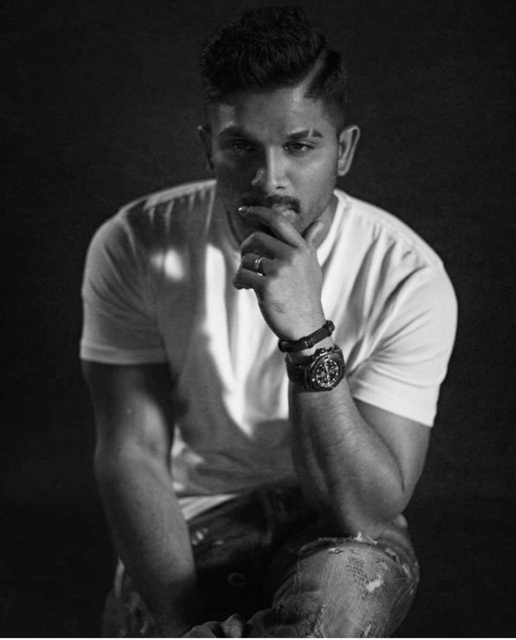 Allu Arjun 桌布 壁紙 — 一個身穿白色T恤和破洞牛仔褲的男人，手托下巴若有所思地擺姿勢的黑白肖像。