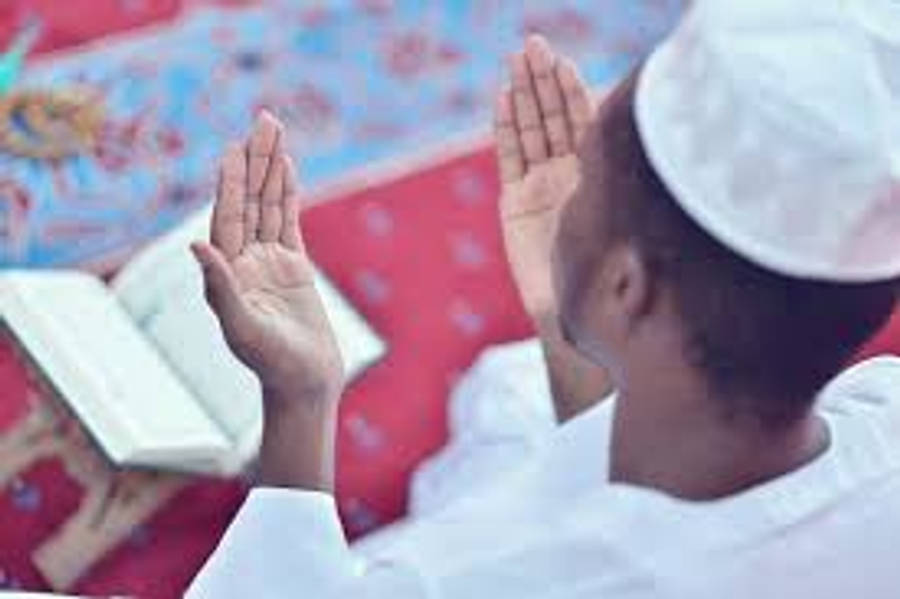 Praying 桌布 壁紙 — 一個身穿白色祈禱服的小男孩在圖案地毯上打開的可蘭經旁邊舉手敬拜。