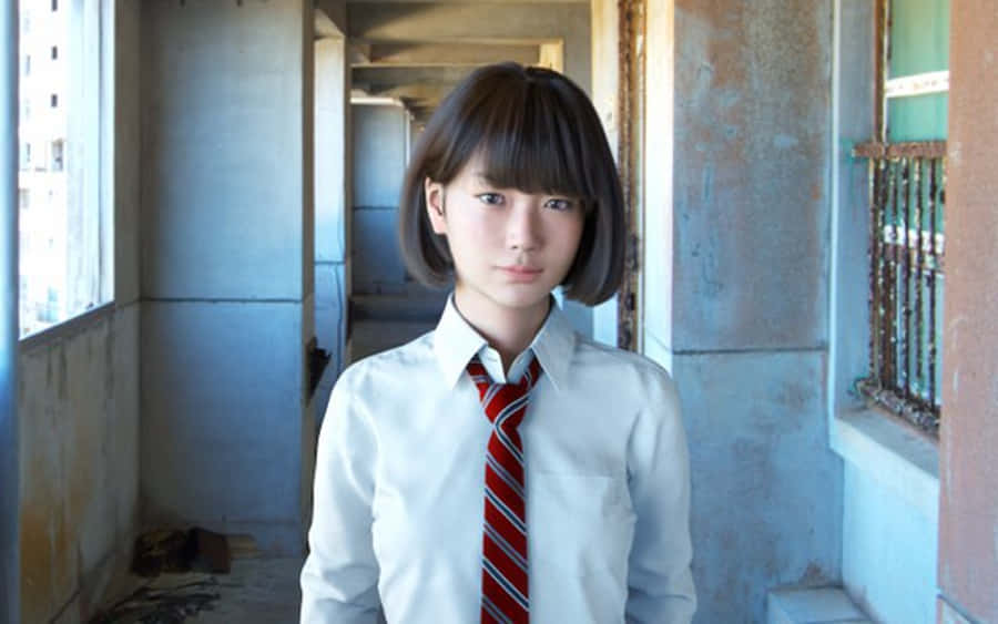 Japanese School Girl 桌布 壁紙 — 一個身穿白襯衫和紅色條紋領帶的小女孩，莊嚴地站在一個牆壁剝落、窗戶破損的破舊走廊裡。