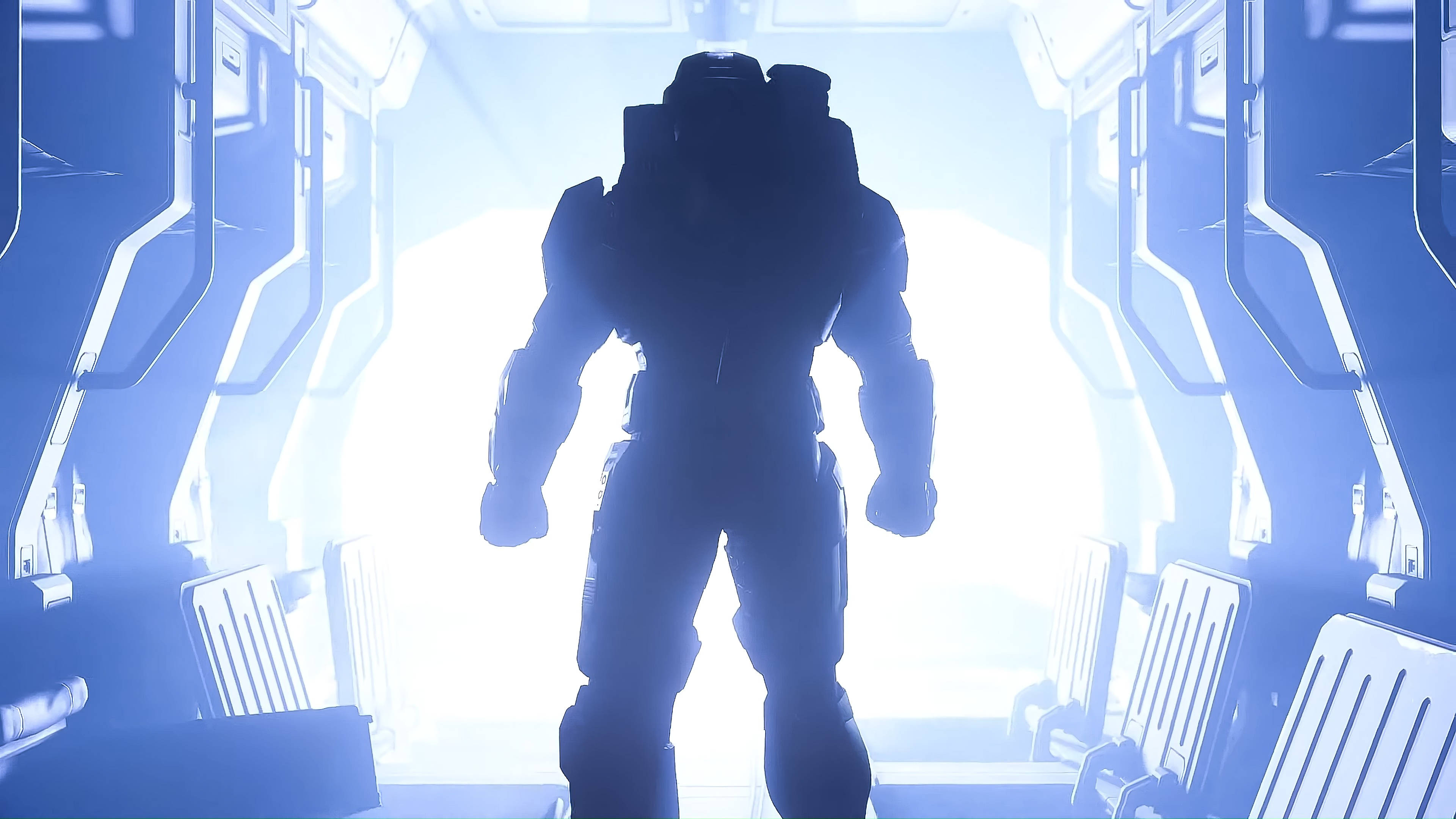 Master Chief 桌布 壁紙 — 一個身穿盔甲的剪影人物站在充滿未來感的太空船走廊中，沐浴在冷藍色的燈光下。