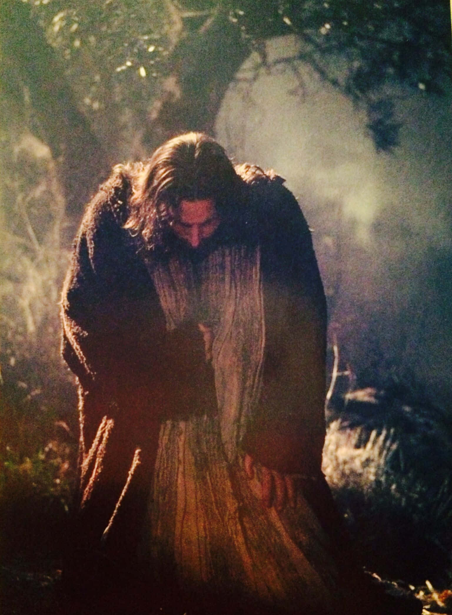 Jesus Praying 桌布 壁紙 — 一個身穿破爛長袍的兜帽身影在沐浴著金色光芒的迷霧森林中鞠躬。