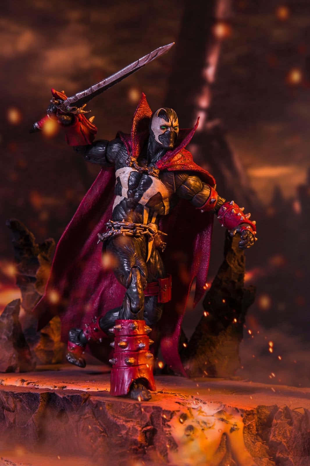 Mortal Kombat 11 Spawn 桌布 壁紙 — 一個身穿紅色披風、手持劍的威嚇裝甲戰士，站在岩石平台上，周圍是熾熱的火花和發光的餘燼。