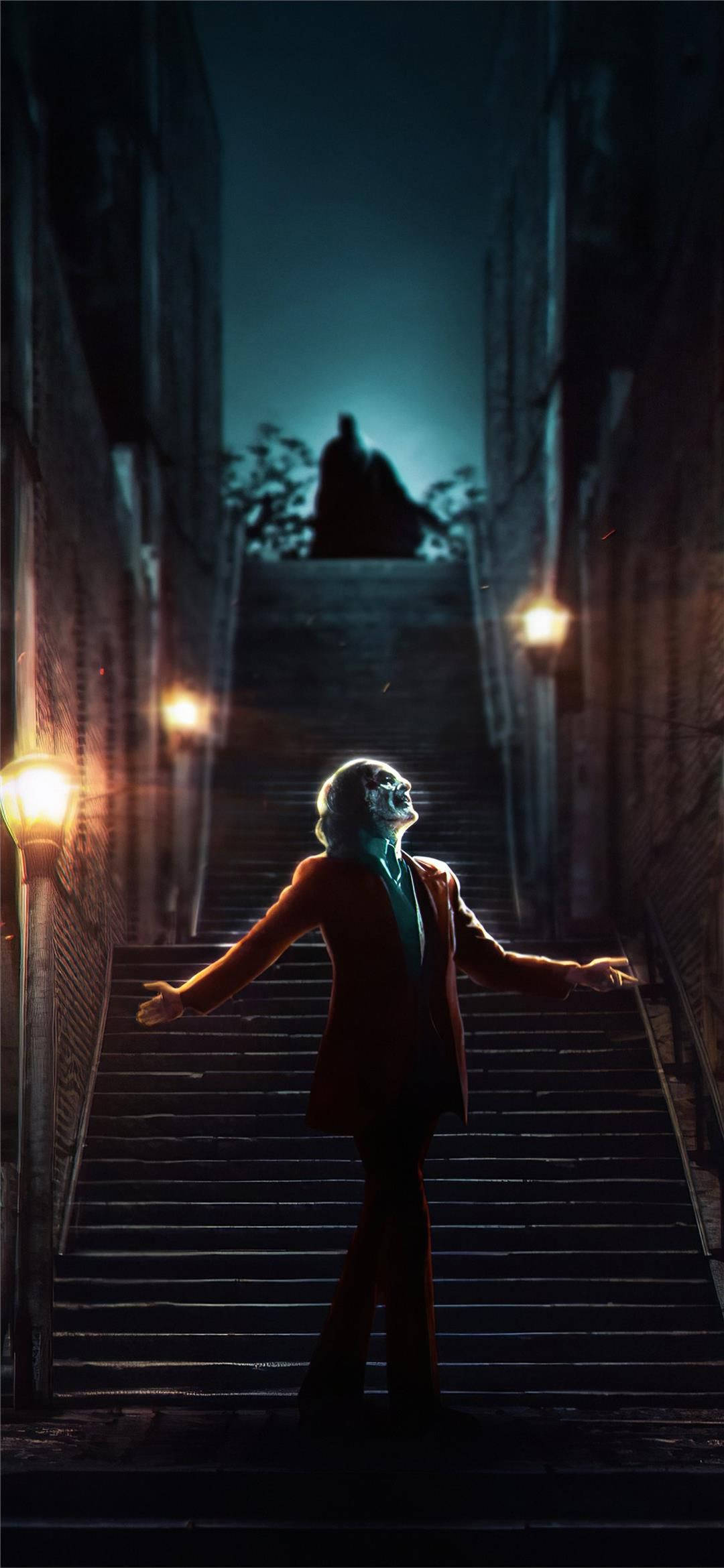 Joker 2019 桌布 壁紙 — 一個身穿紅色西裝的人站在昏暗的石樓梯底部，雙臂張開，而一個陰影輪廓在頂部青綠色的天空下若隱若現。