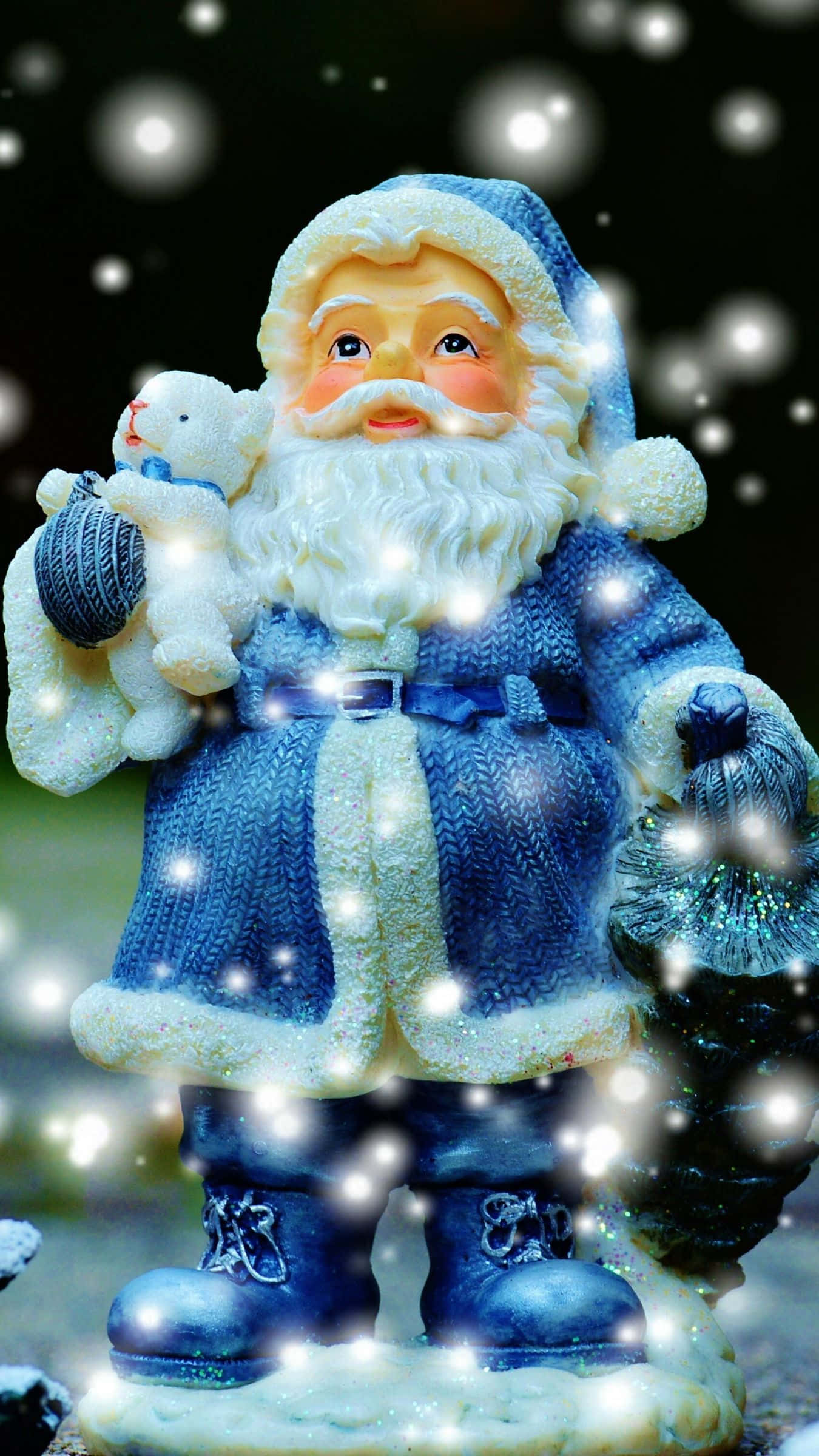 Santa Claus HD 桌布 壁紙 — 一個身穿藍色衣服、笑容滿面的聖誕老人公仔，在閃閃發光的雪景背景下，抱著一隻泰迪熊和一個毛線球。