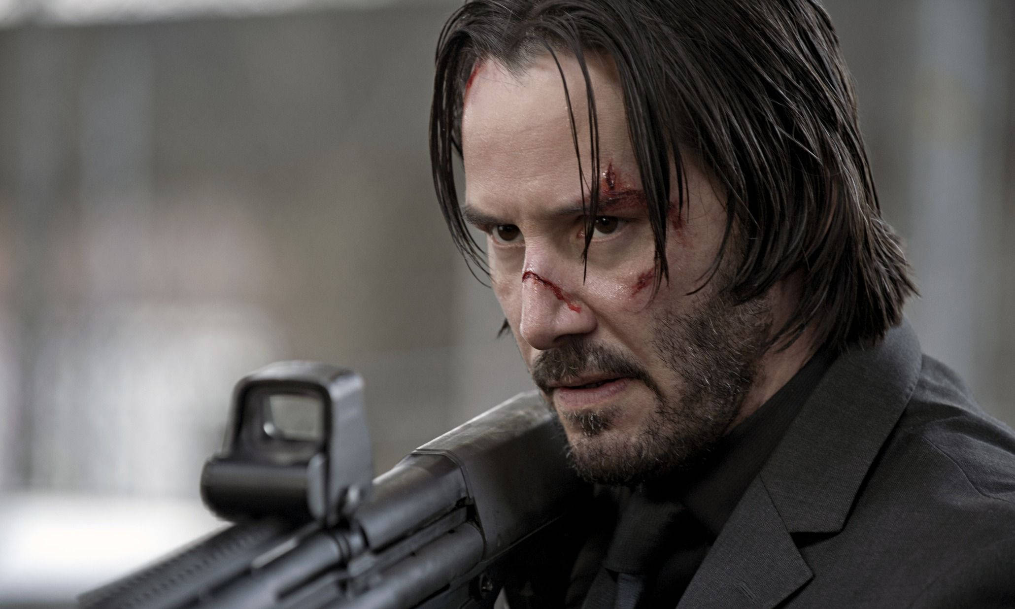 Keanu 桌布 壁紙 — 一個身穿西裝、血跡斑斑的男人，專注地瞄準步槍的 gritty 特寫。