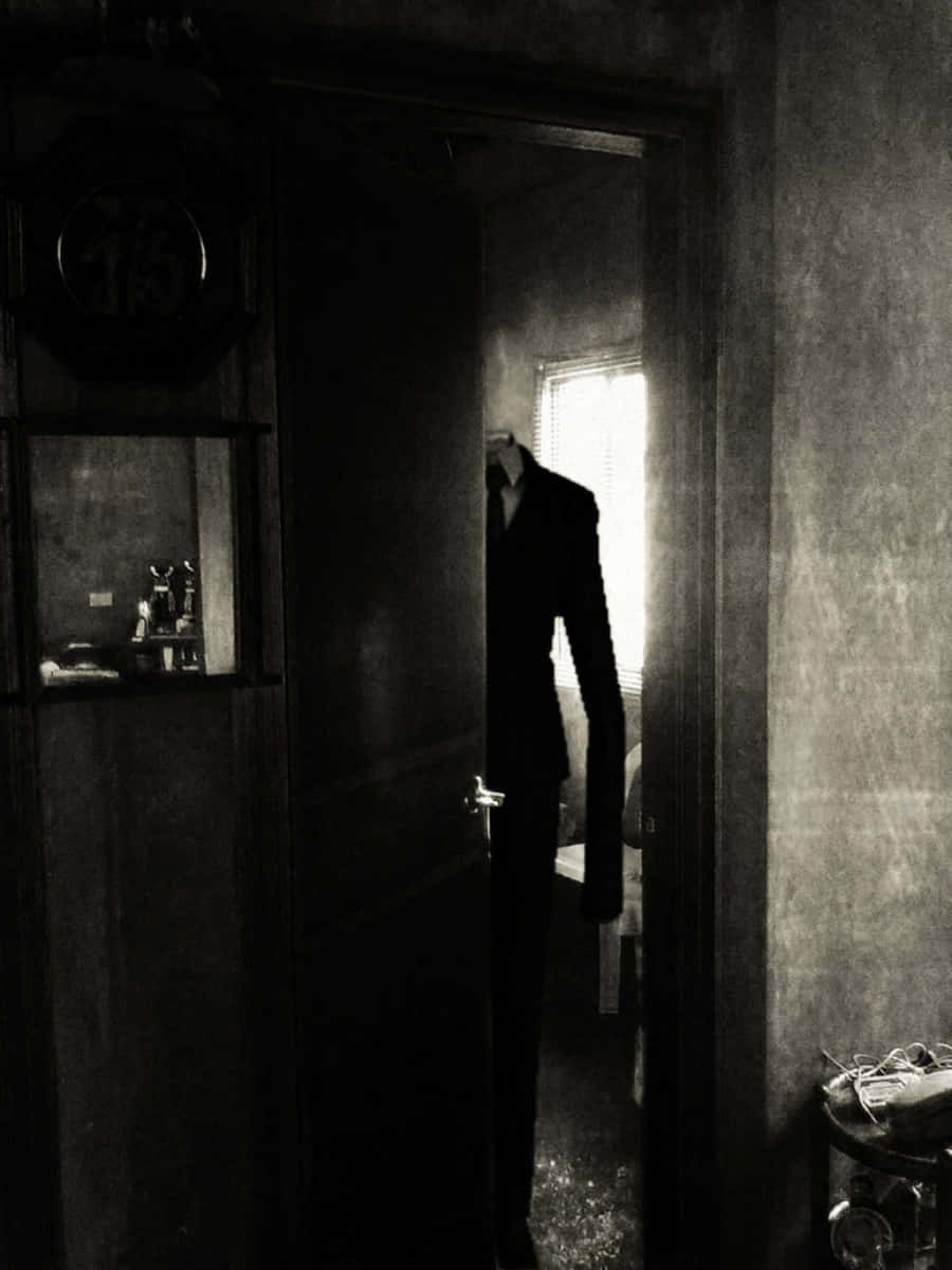Creepypasta 桌布 壁紙 — 一個身穿西裝的高瘦身影站在昏暗的門口，無頭的剪影被背後窗戶的光線框住。