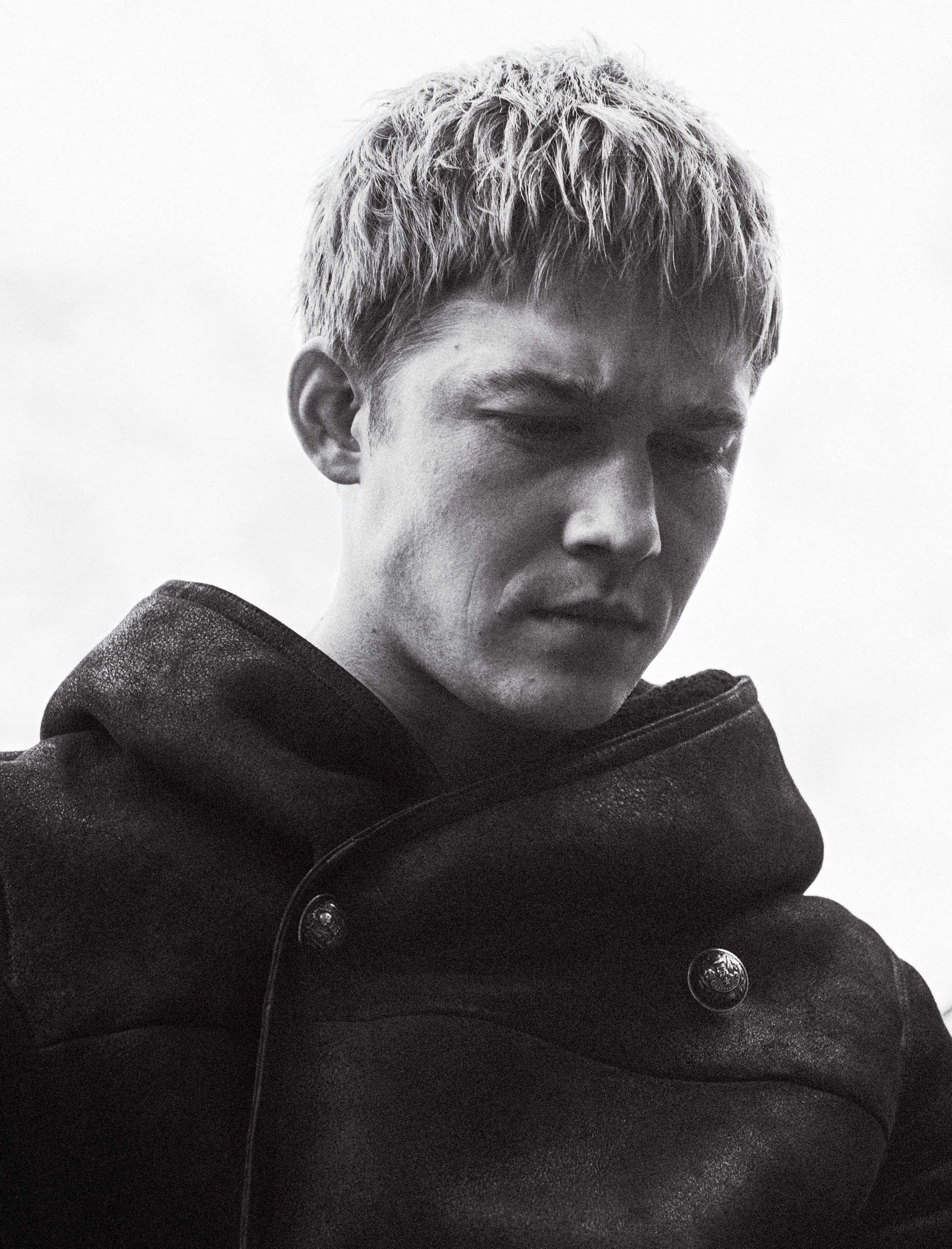 Joe Alwyn 桌布 壁紙 — 一個身穿質感外套、頭髮蓬亂的年輕男子低頭看的黑白肖像。