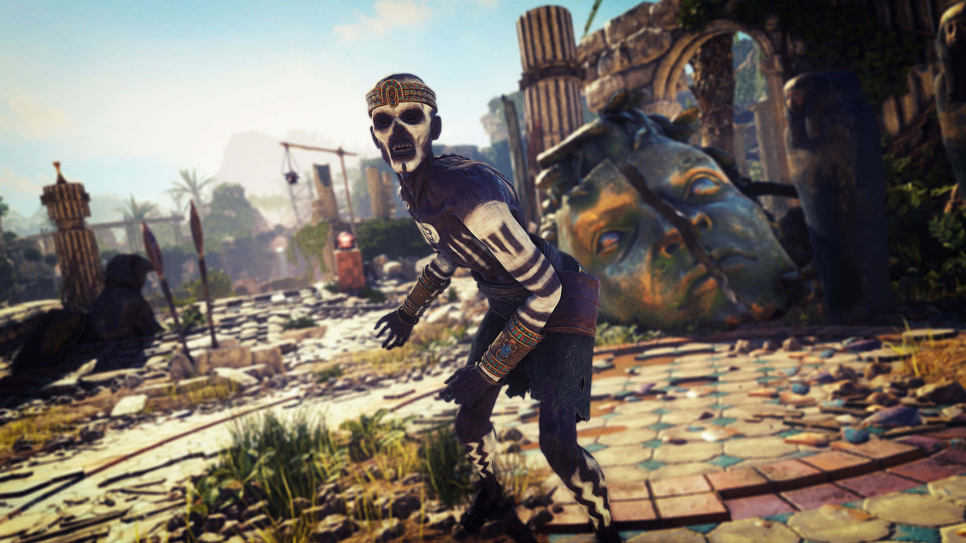 1920x1080 Strange Brigade 桌布 壁紙 — 一個身穿部落盔甲的骷髏戰士，在陽光明媚的廢墟中，伴隨著巨大的石頭頭顱和破碎的柱子，威風凜凜地站立著。