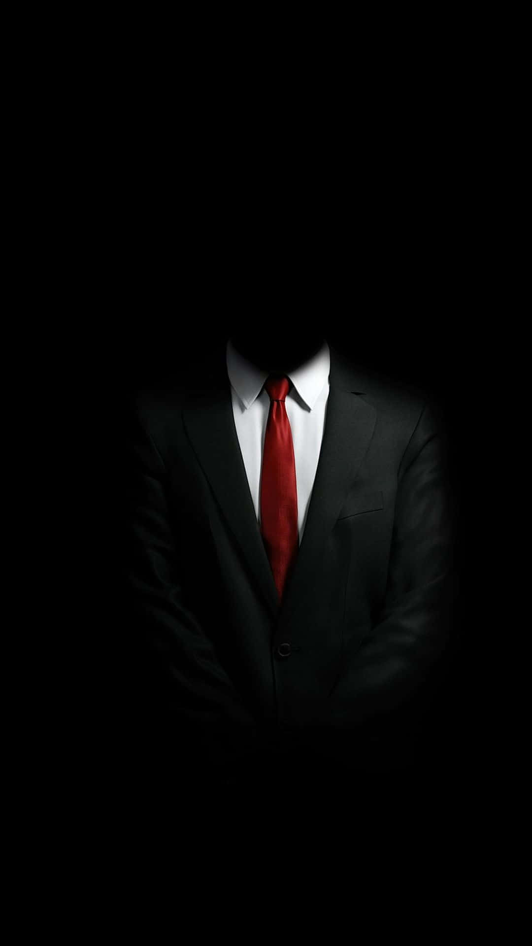 suit 桌布 壁紙 — 一個身穿黑色西裝和紅色領帶的人物站在黑暗中，沒有可見的臉，營造出神秘和不祥的存在感。