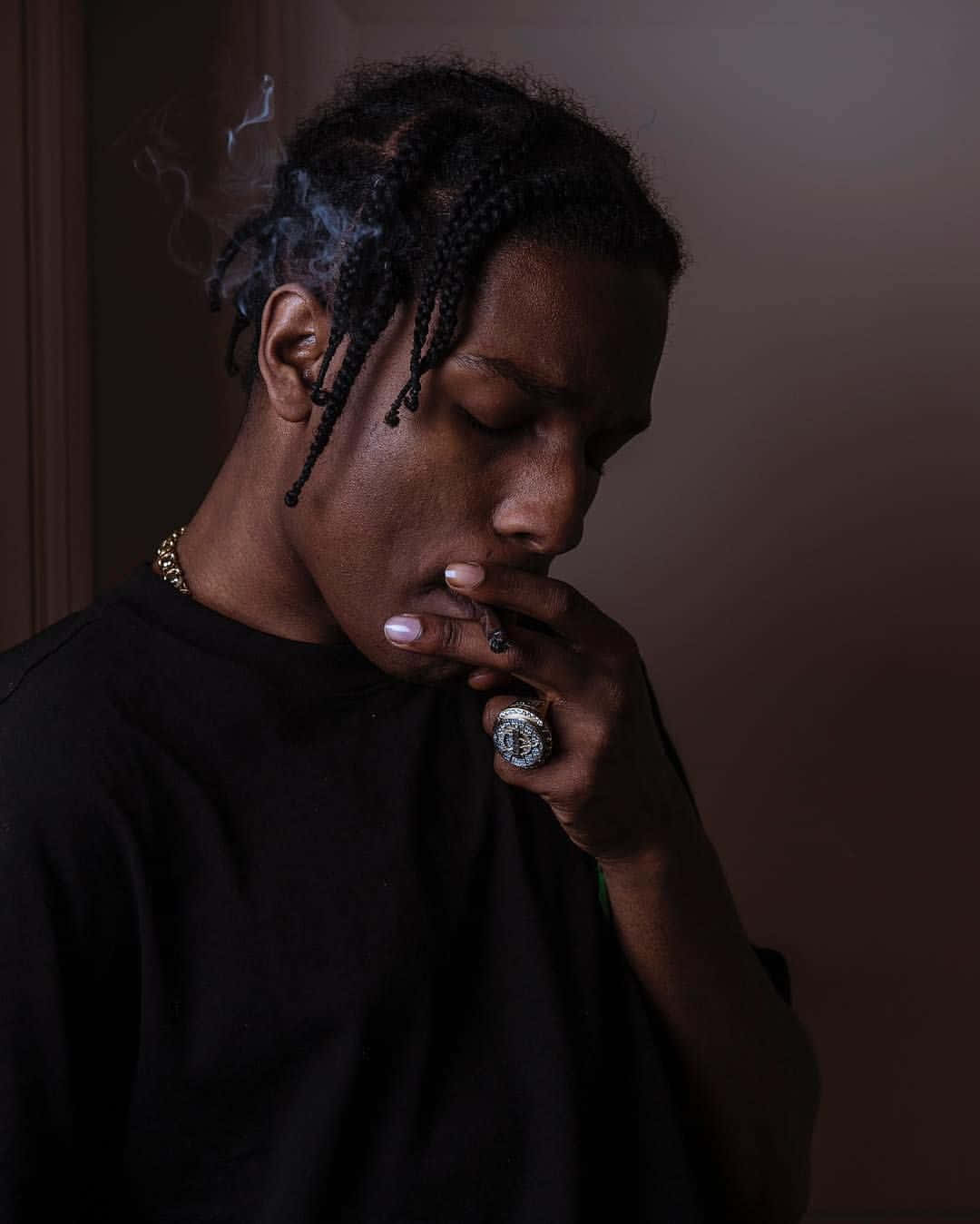 ASAP Rocky 桌布 壁紙 — 一個辮子男人在昏暗的房間裡拿著香煙呼出煙霧。