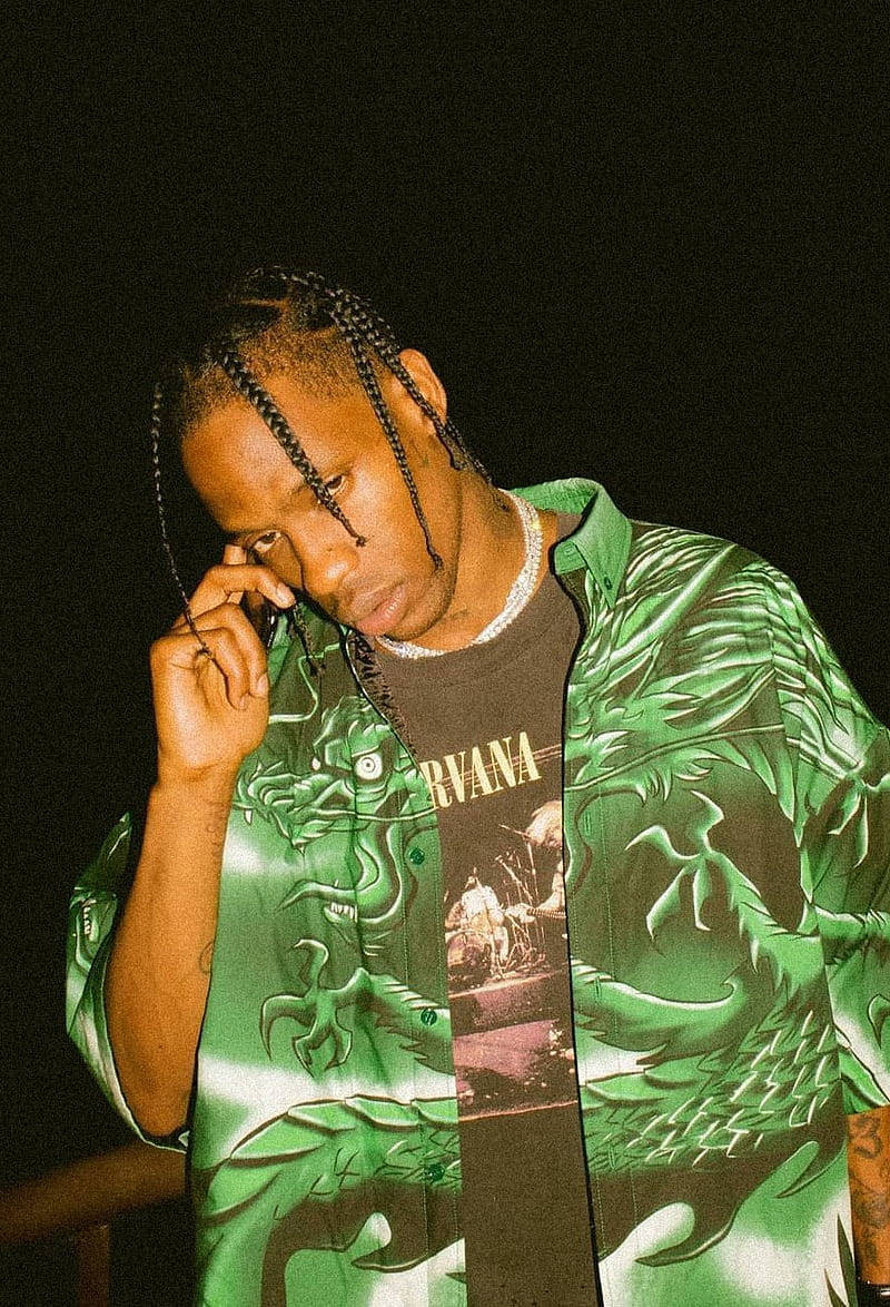 Travis Scott Aesthetic 桌布 壁紙 — 一個辮子頭的男人穿著綠色龍紋襯衫，在深色背景前將電話貼在耳邊。