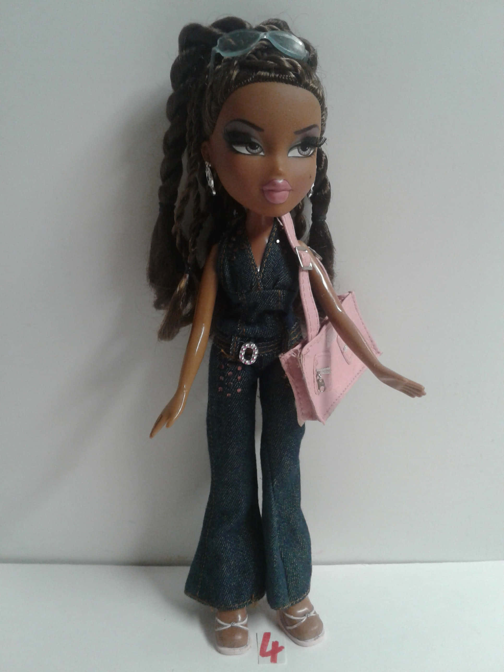 bratz 美學 桌布 壁紙 — 一個辮子頭髮、頭上戴著太陽眼鏡的 Bratz 公仔，身穿牛仔服，手持粉紅色手袋。