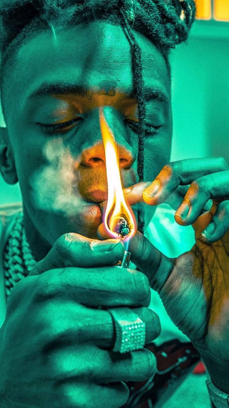 Jaydayoungan 桌布 壁紙 — 一個辮子頭髮的人在青綠色燈光下用打火機點燃大麻煙，同時呼出煙霧。