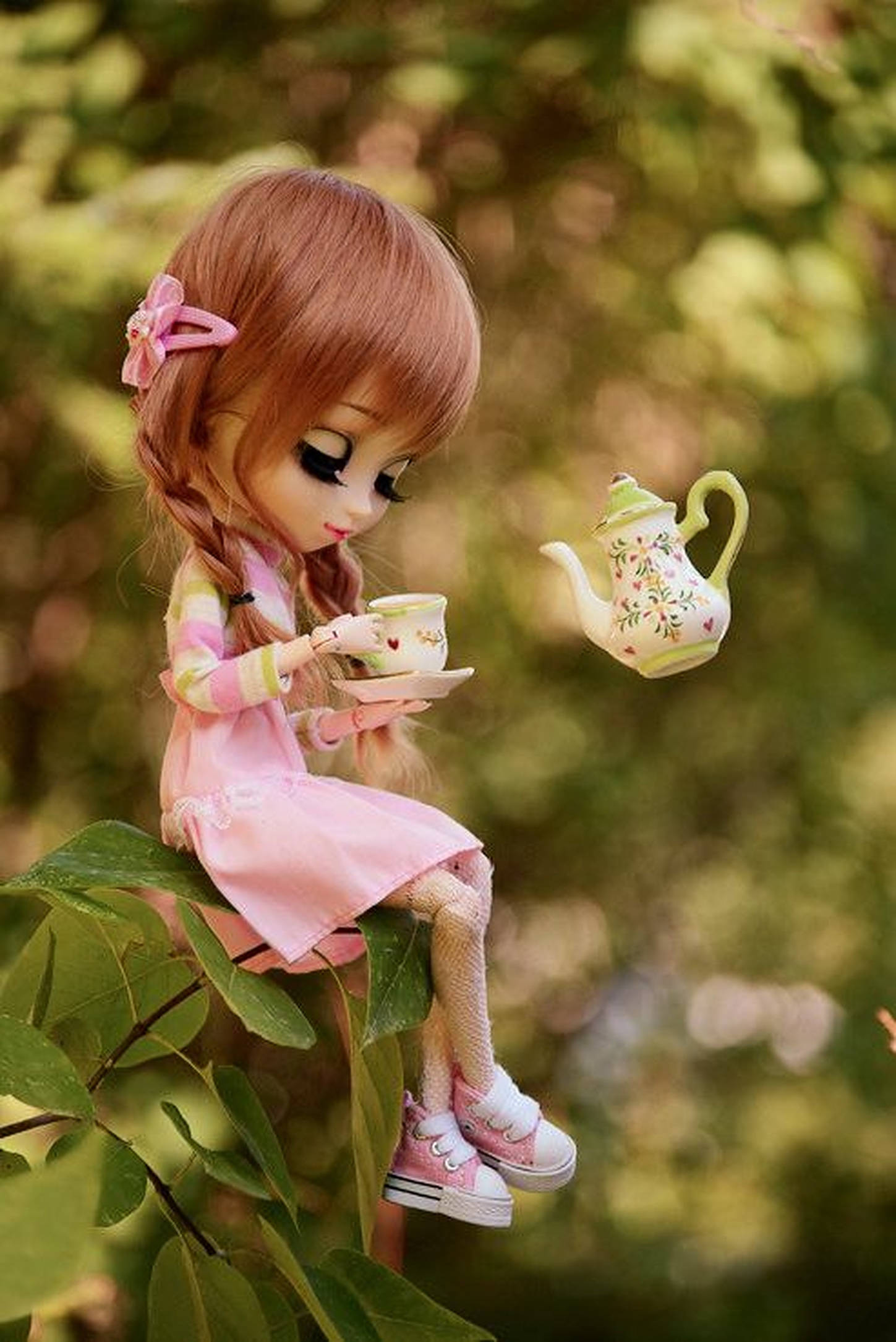 Doll 桌布 壁紙 — 一個辮子頭髮的洋娃娃坐在長滿樹葉的樹枝上喝茶，一個花茶壺在陽光普照的花園裏飄浮在她身邊。
