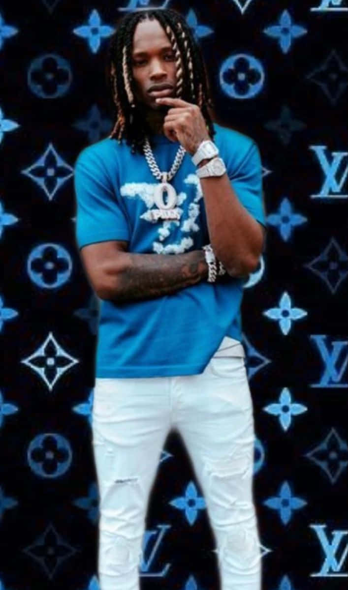 辮子男人穿著藍色襯衫和白色褲子，在LV圖案背景前。 — King Von 壁紙