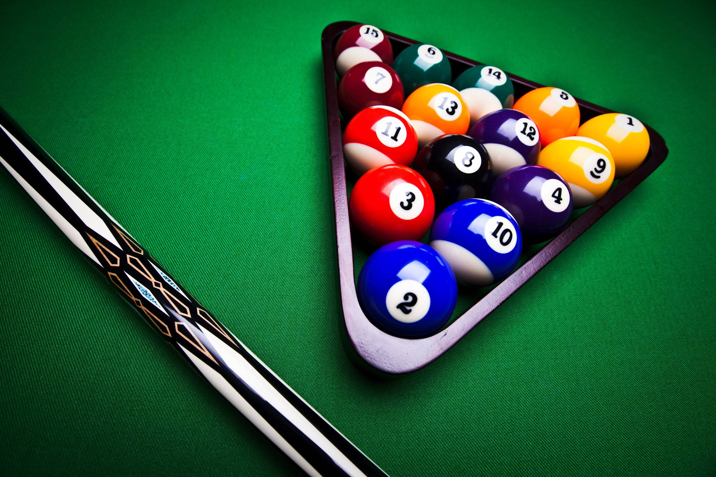 Snooker 桌布 壁紙 — 一個近距離拍攝，撞球桿擱在一個裝有色彩繽紛、帶有號碼的撞球球的架子旁邊，放在一張充滿活力的綠色絨布桌上。