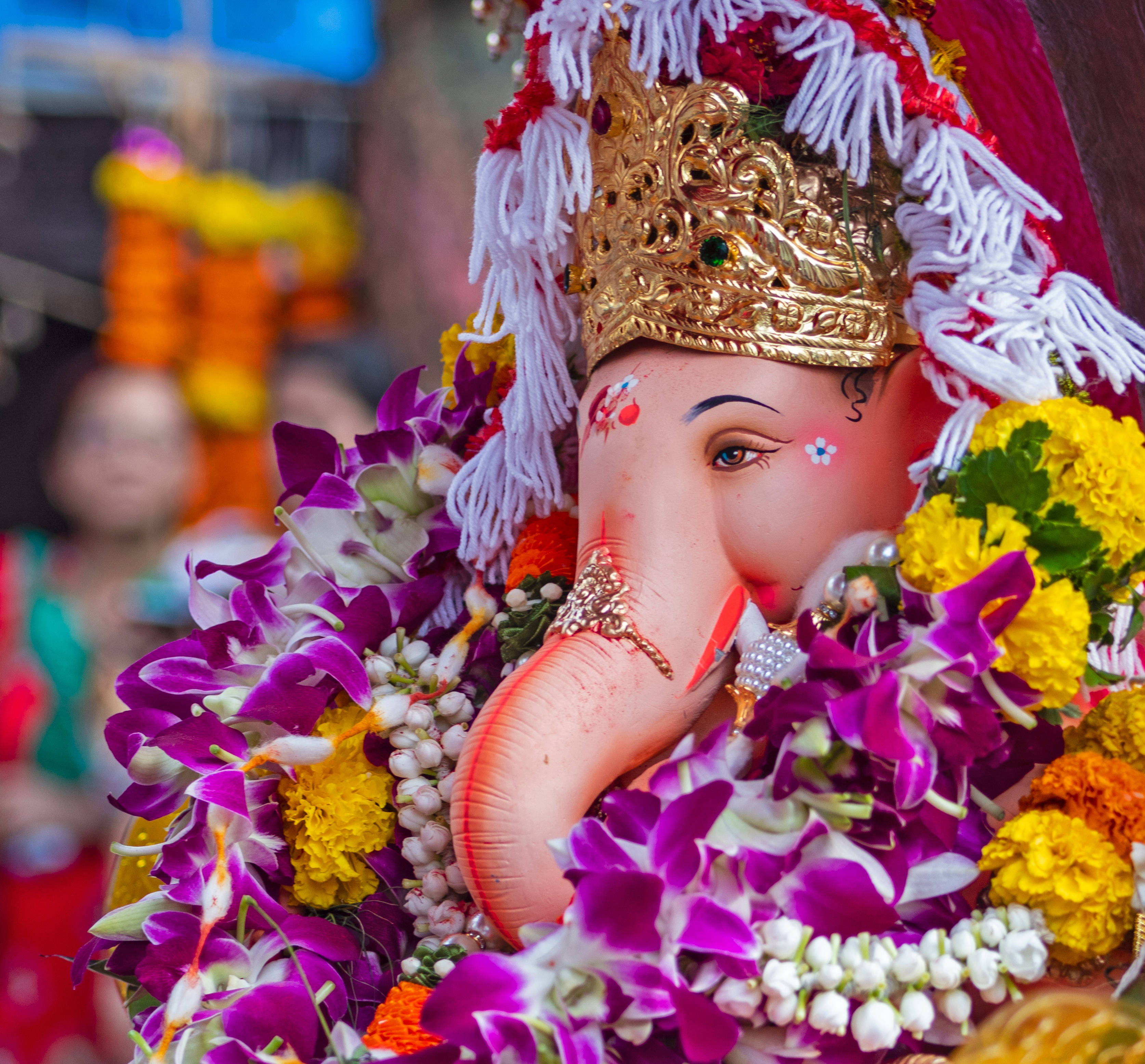 Bappa 桌布 壁紙 — 一個近距離拍攝的裝飾華麗的象頭神像，飾有紫色、黃色和白色的花朵以及金色皇冠。