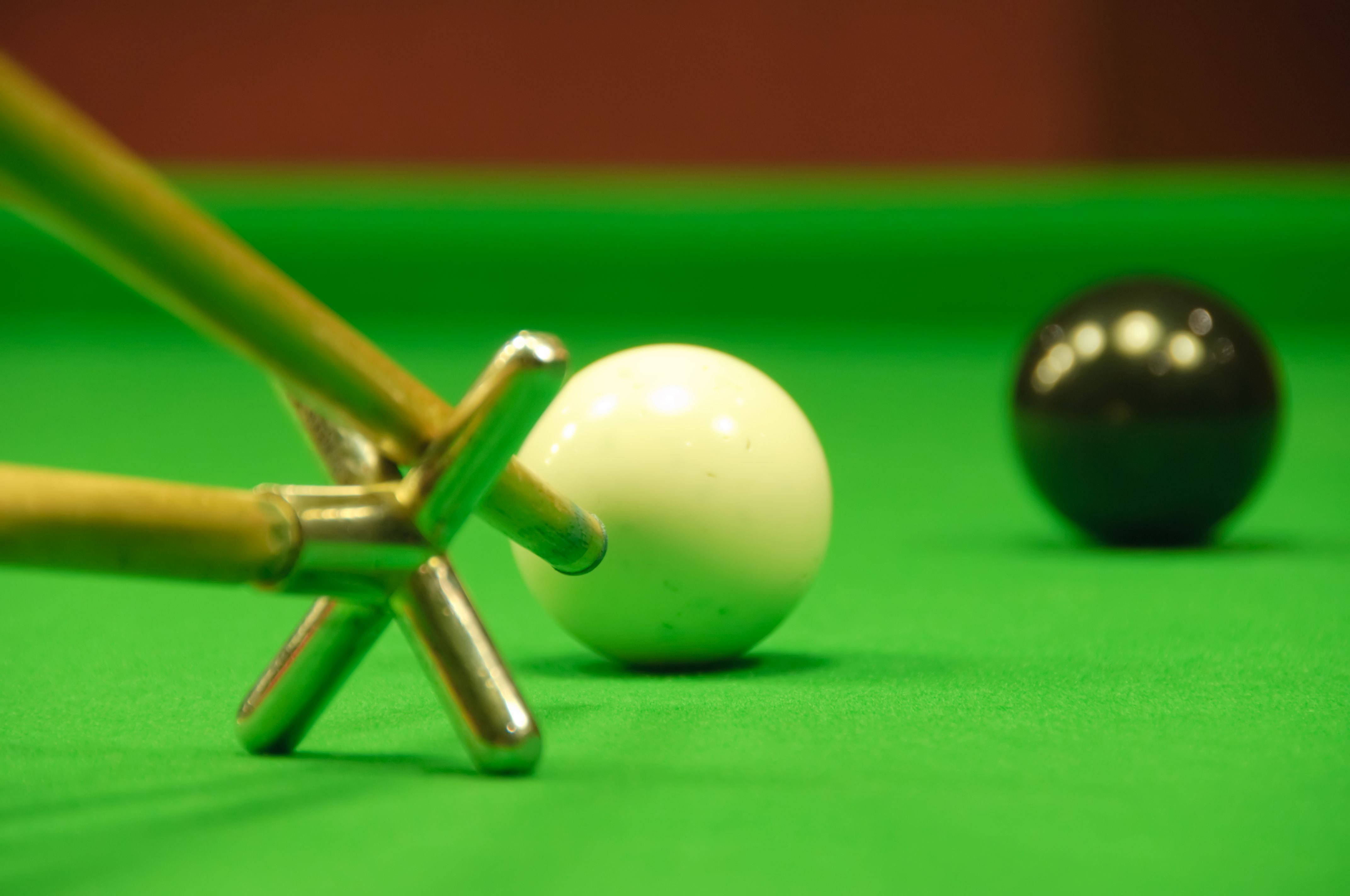Snooker 桌布 壁紙 — 一個近距離特寫，顯示一支撞球桿放在白色球上，背景有一個黑色球模糊，在充滿活力的綠色絨布桌上。