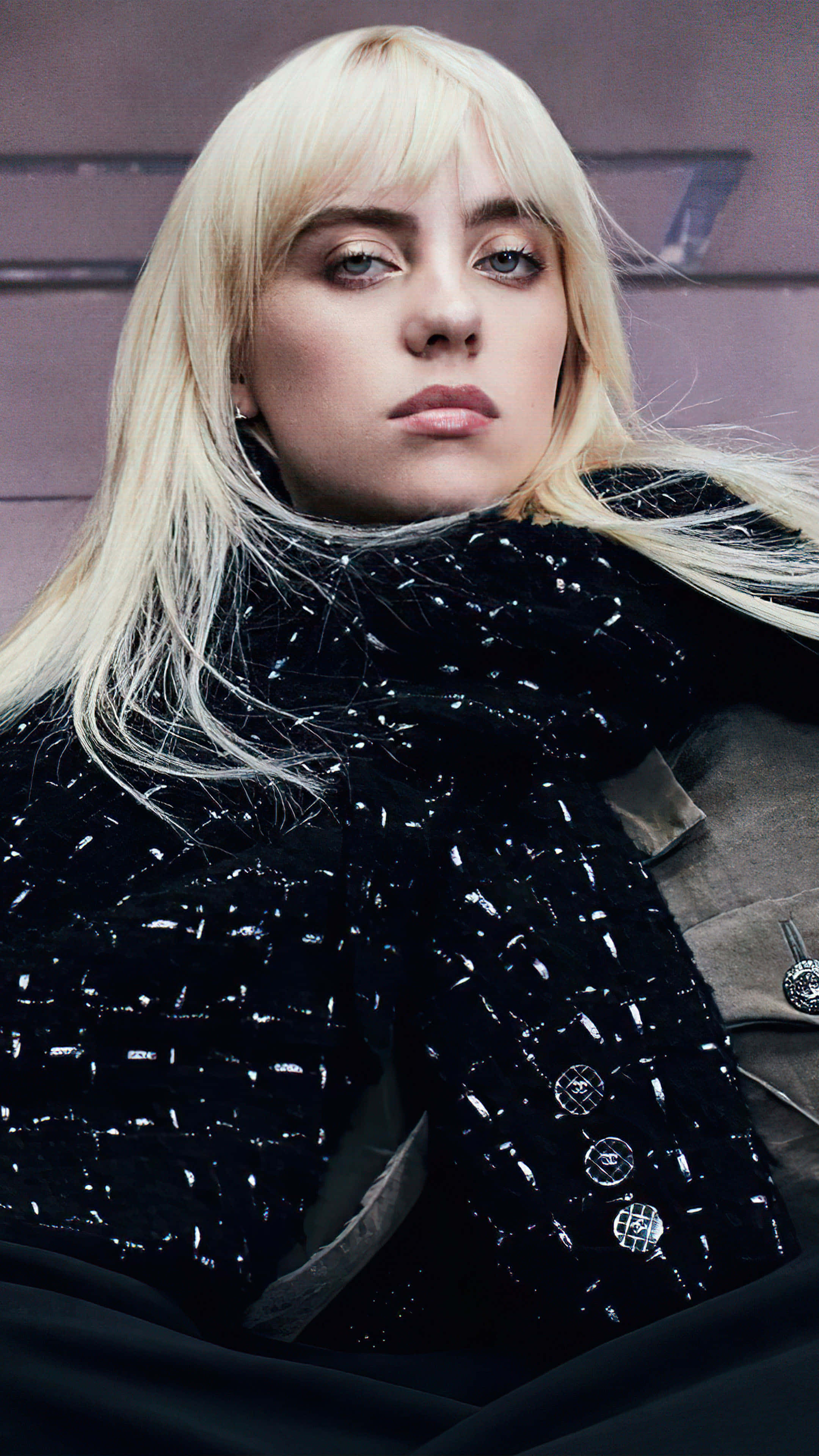 Billie Eilish 2021 桌布 壁紙 — 一個近距離肖像，一位金髮女子眼神強烈，穿著質感黑色外套，背景是柔和的紫色牆壁。