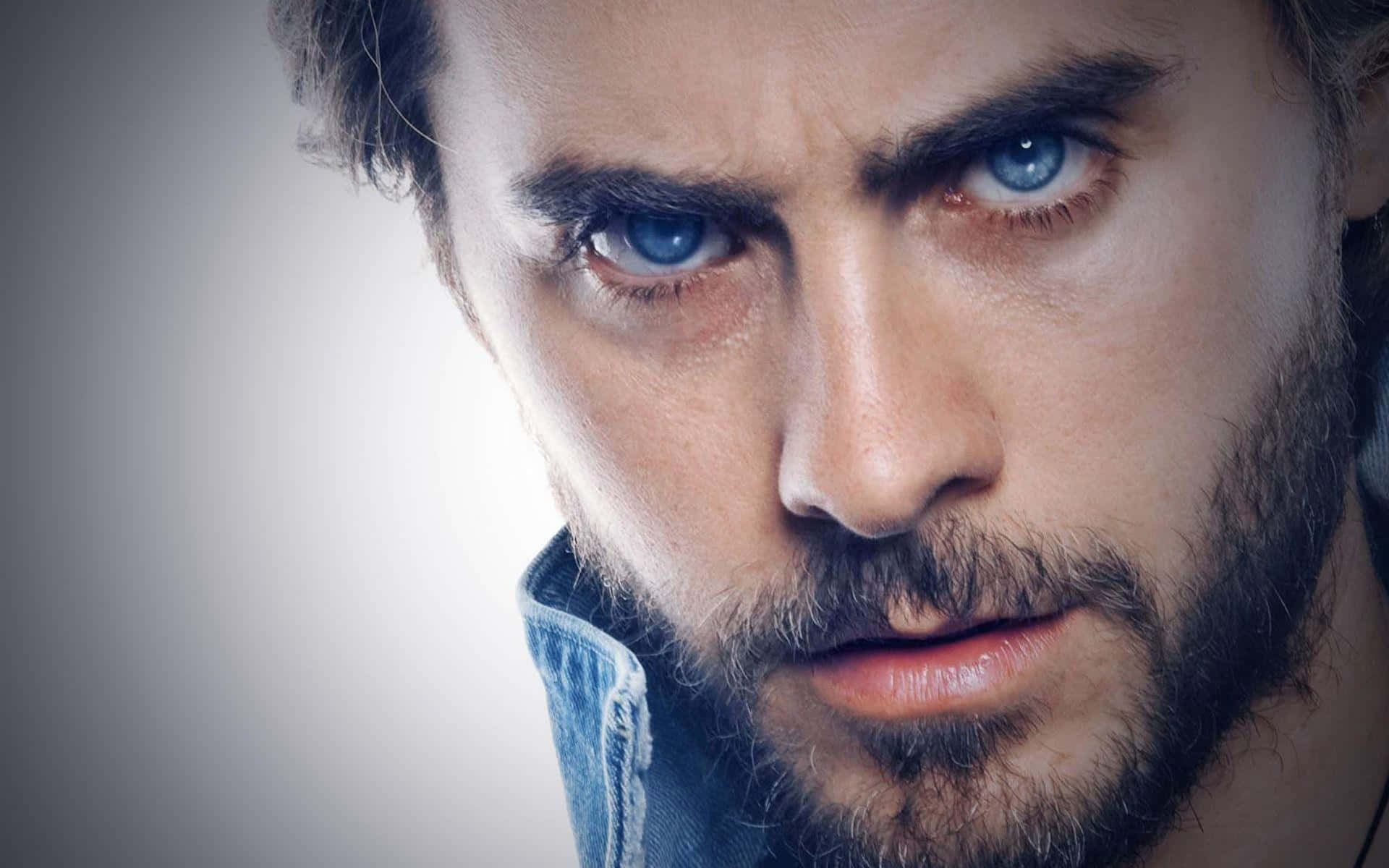 jared leto 桌布 壁紙 — 一個近距離肖像，一個擁有強烈藍色眼睛和鬍鬚的男人，直視鏡頭，背景是柔和的灰色。