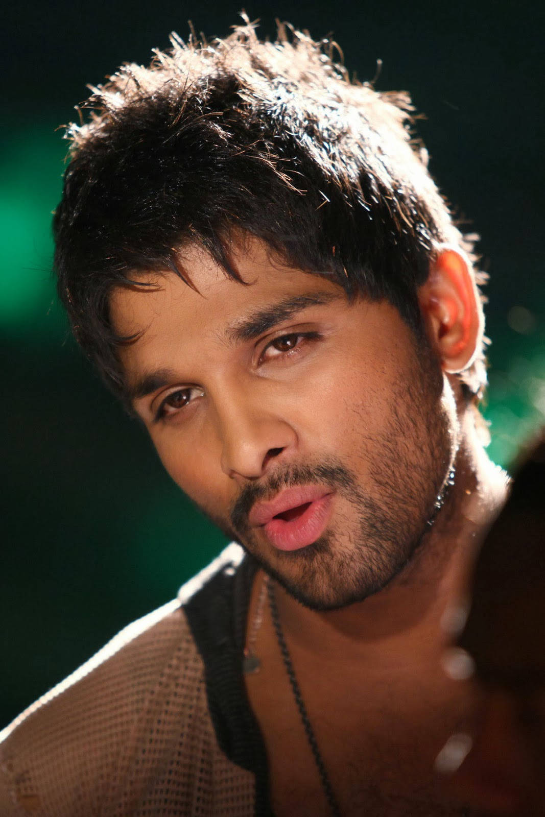 Allu Arjun 桌布 壁紙 — 一個近距離肖像，一個深色亂髮和鬍渣的男人在戲劇性的綠色燈光下強烈地看著相機。
