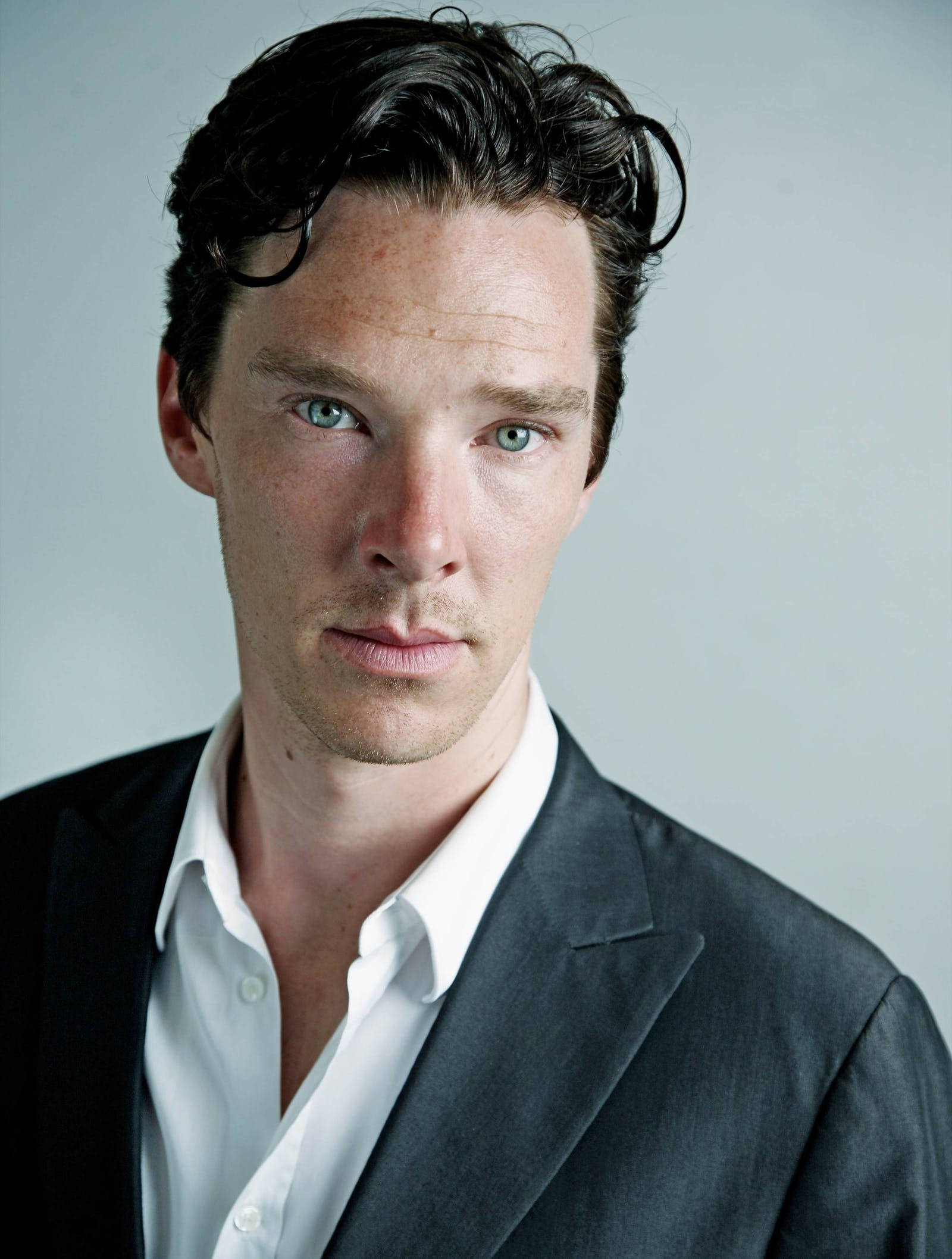 benedict 桌布 壁紙 — 一個近距離肖像，一個男人擁有強烈的藍眼睛和深色頭髮，穿著黑色西裝和白色襯衫，背景是純灰色。