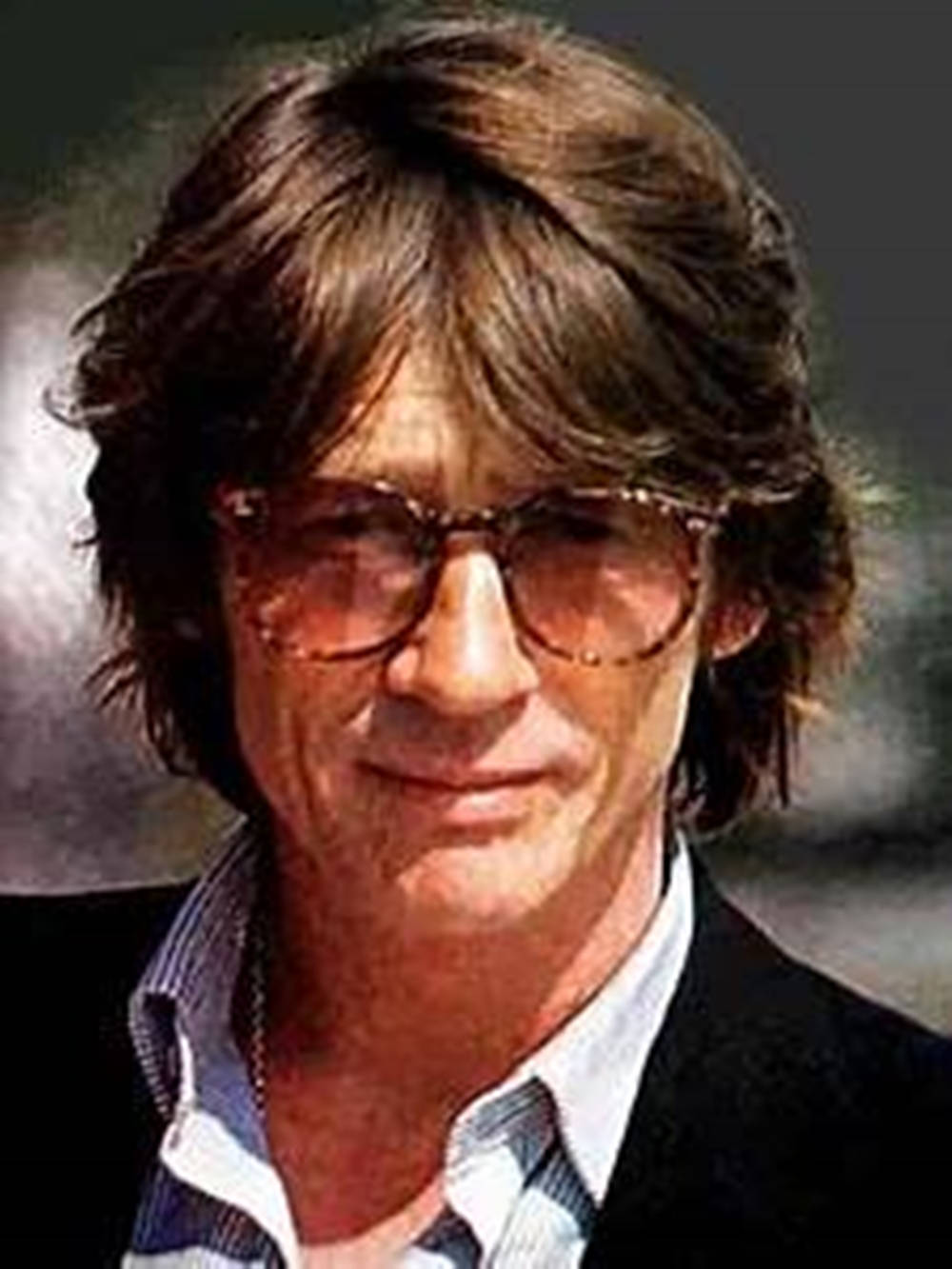 glasses 桌布 壁紙 — 一個近距離肖像，一個男人有著凌亂的棕色頭髮和大型圓形太陽眼鏡，對著鏡頭溫柔微笑。