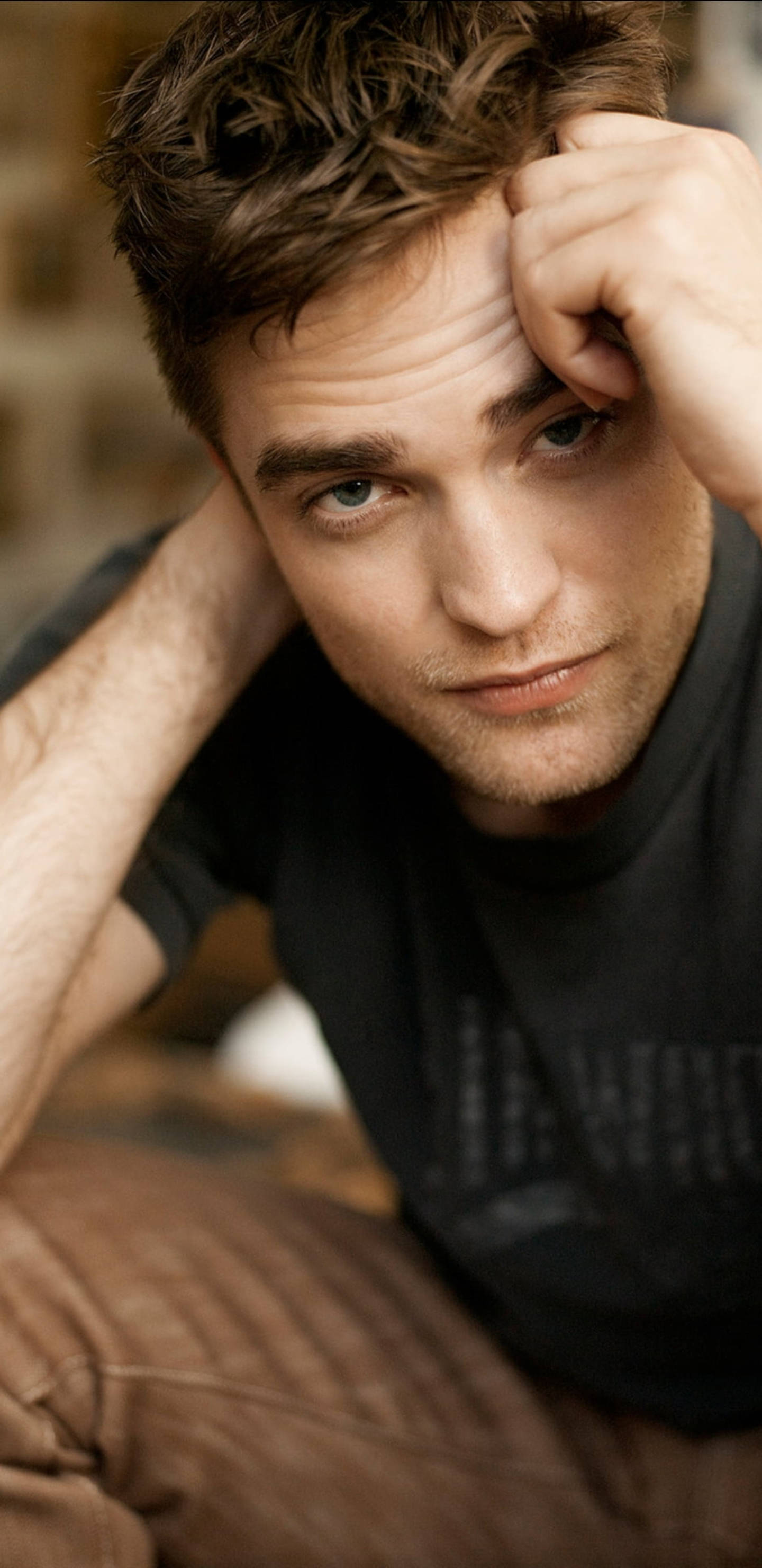 Robert Pattinson 桌布 壁紙 — 一個近距離肖像，一個男人有著凌亂的棕色頭髮和強烈的藍色眼睛，將頭靠在手上。