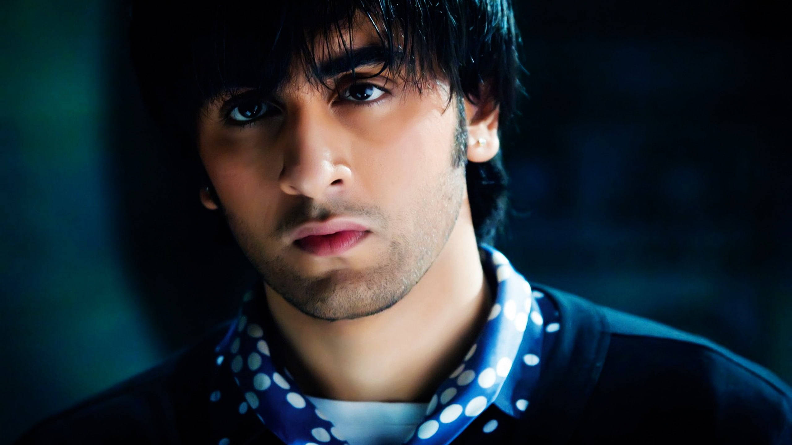 Ranbir Kapoor 桌布 壁紙 — 一個近距離肖像，一個黑髮、眼神銳利的男人，在戲劇性的藍色燈光下戴著藍色圓點圍巾。