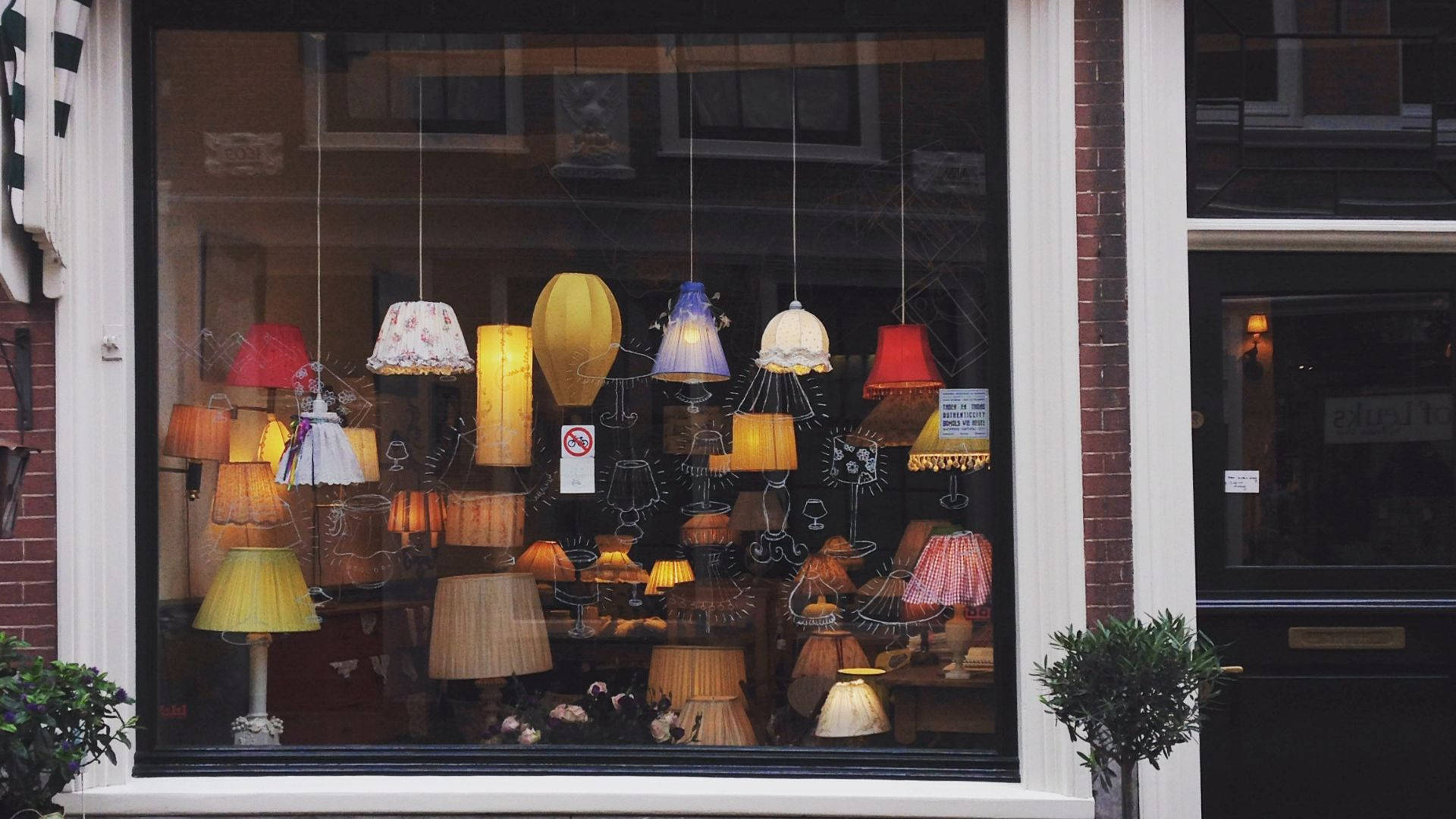 window 桌布 壁紙 — 一個迷人的商店櫥窗展示了一系列色彩繽紛的吊燈和立燈，燈罩帶有圖案，背景是磚砌建築外牆。