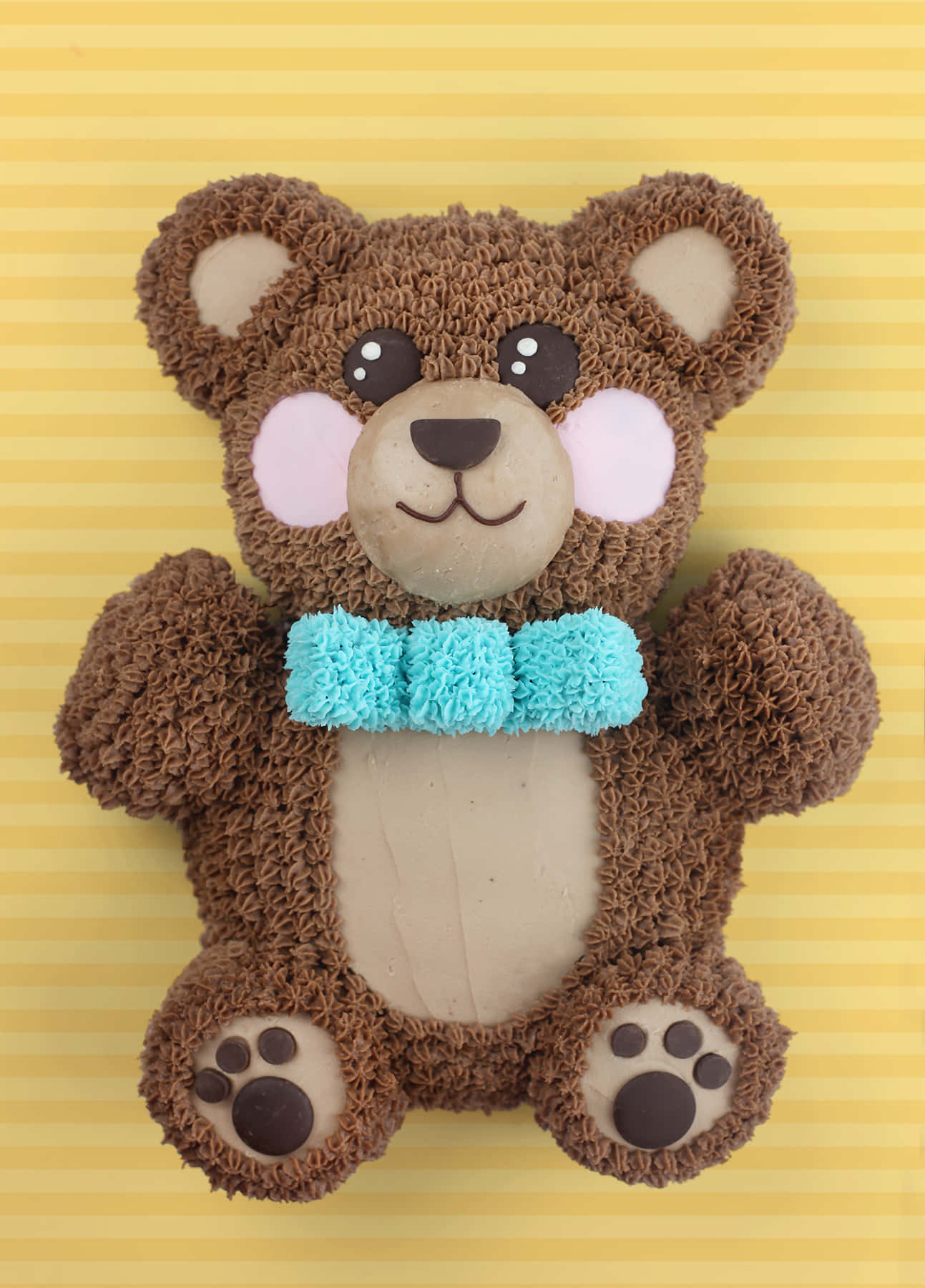 Teddy Bear 桌布 壁紙 — 一個迷人的泰迪熊蛋糕，帶有紋理的棕色糖霜和一條藍綠色蝴蝶結，背景是黃色條紋。